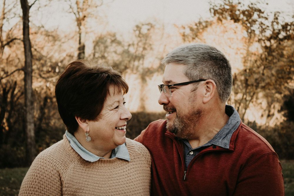 A candid image of a man and a woman seated and smiling at each other. There is a sunset in the background.