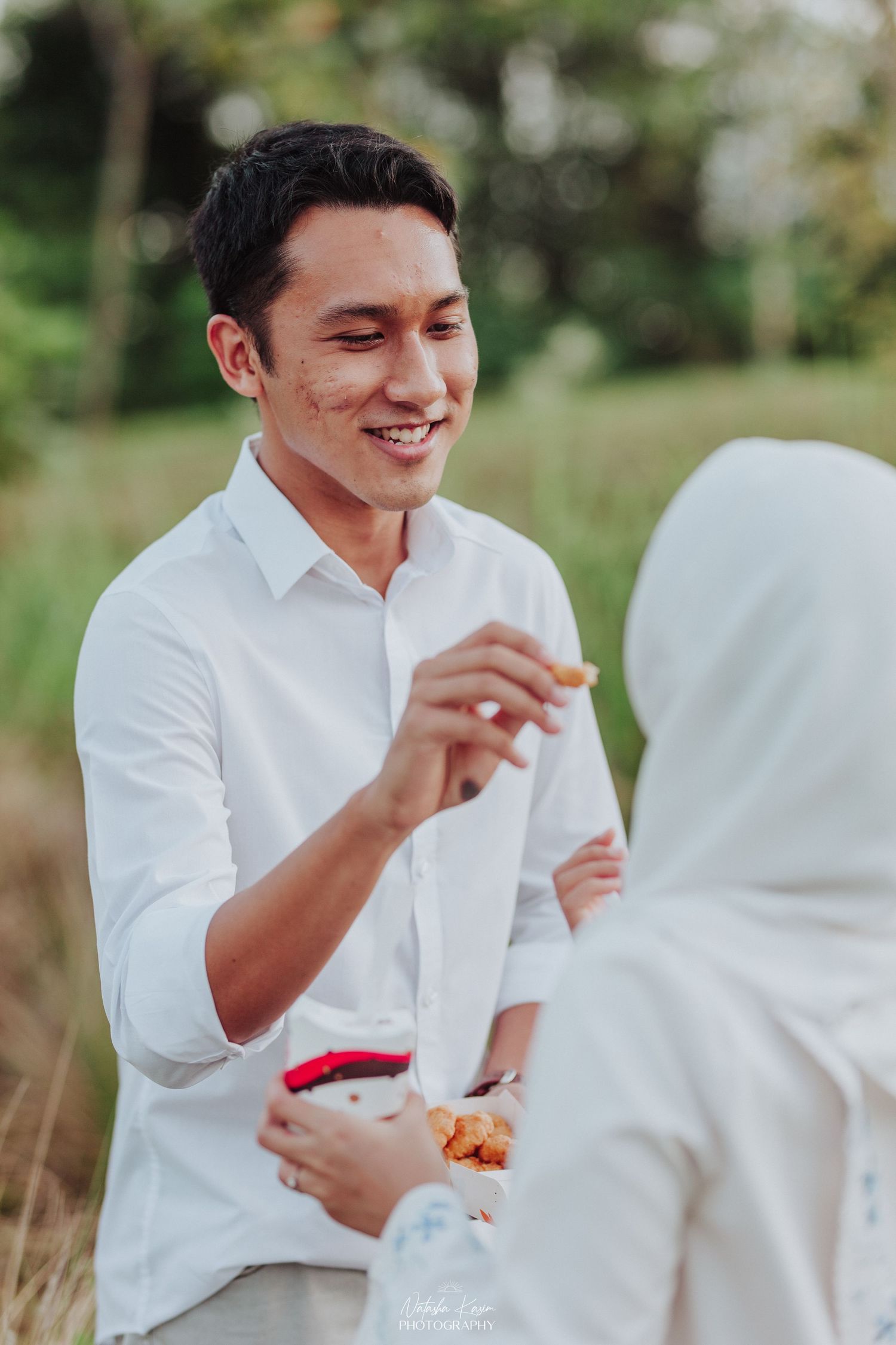 A couple shares a lighthearted moment while enjoying snacks in an outdoor setting.
