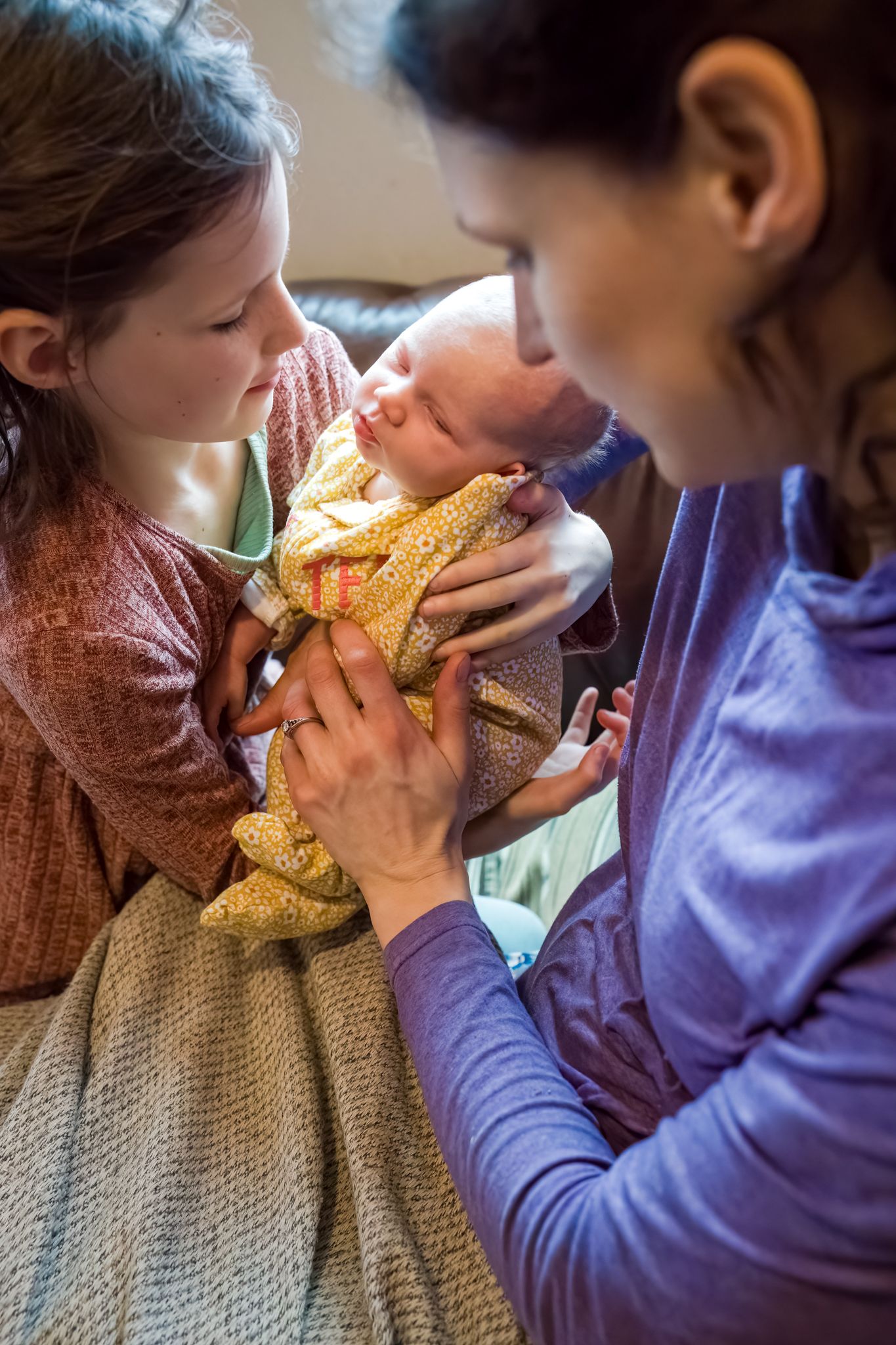 mom handing baby girl to big sister