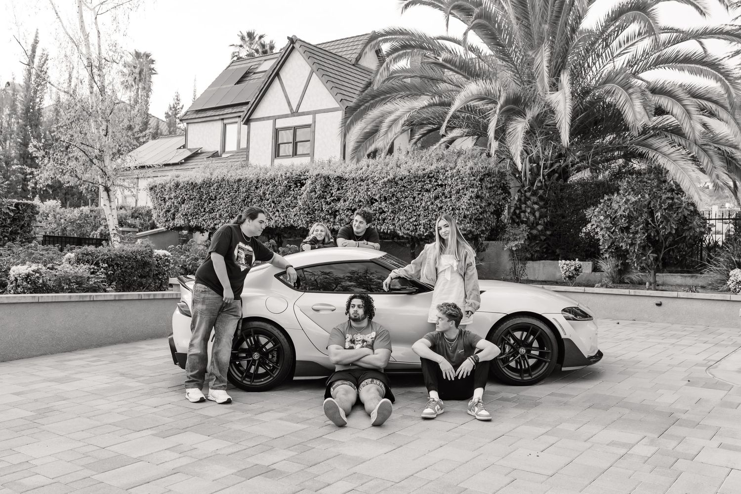 High school students surrounding a sportscar.  Some are leaning on the car and others are standing against the car.