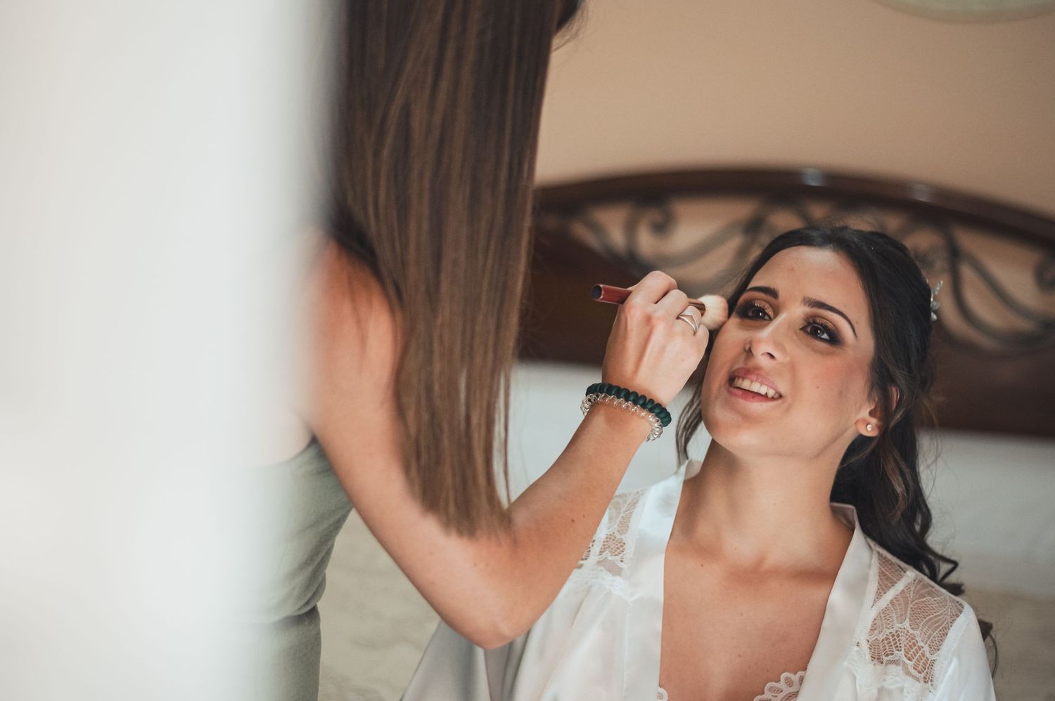 Makeup artist carefully applies eye makeup to someone in a white lace trimmed robe.