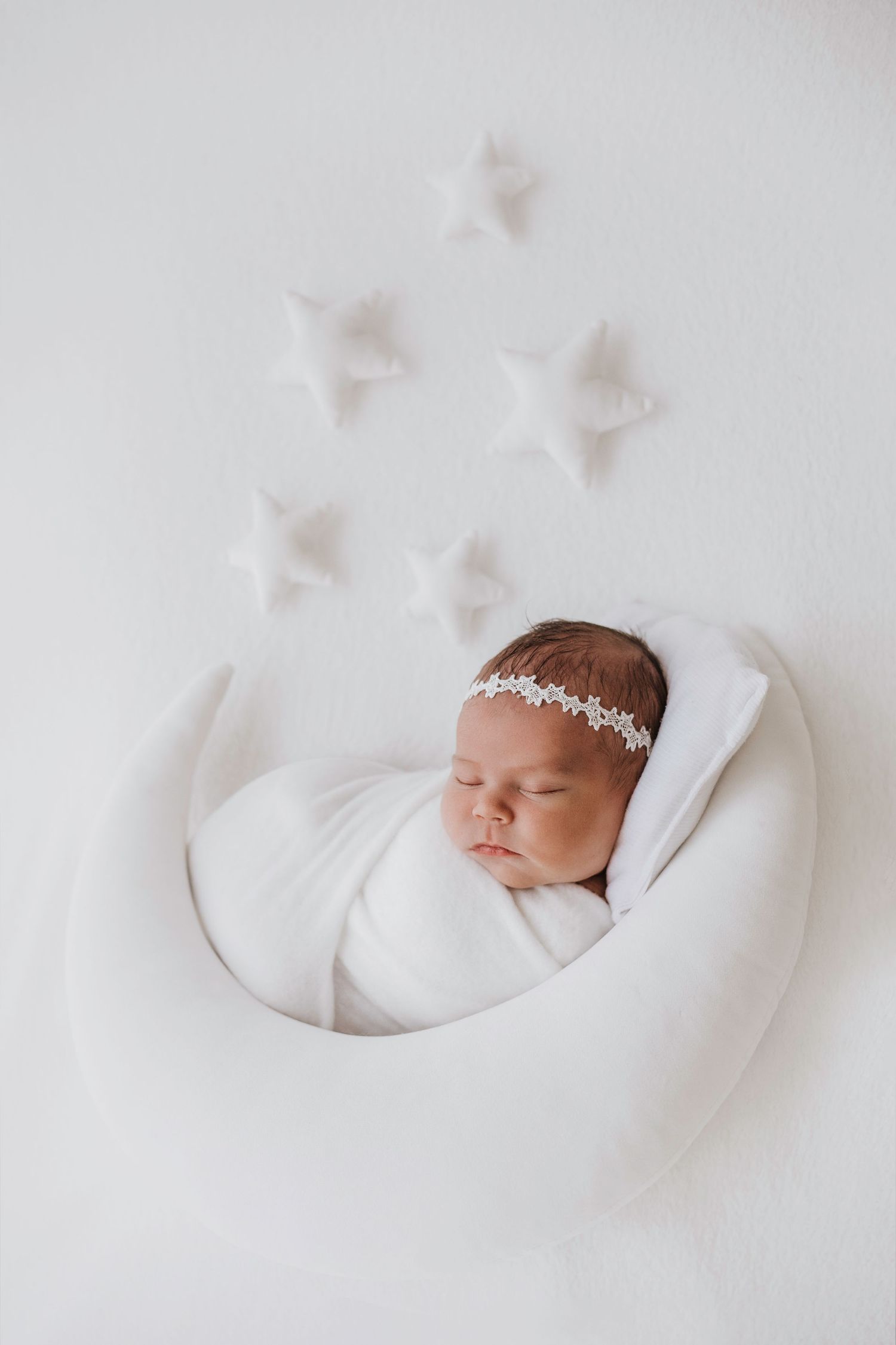 A sleeping newborn wrapped in white with decorative stars above in minimal setting.