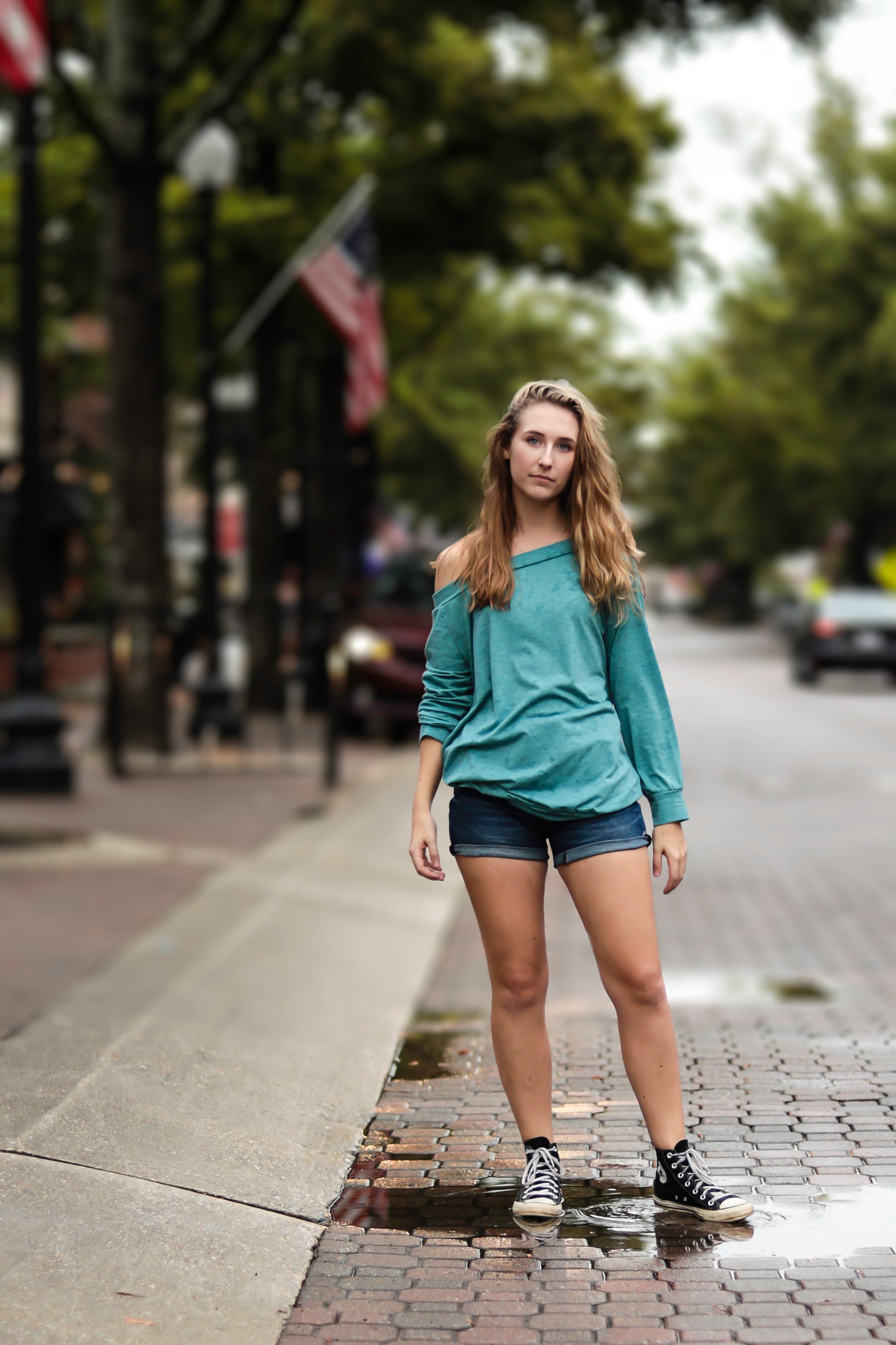 Street style portrait on a brick sidewalk with American flags visible in the urban background.