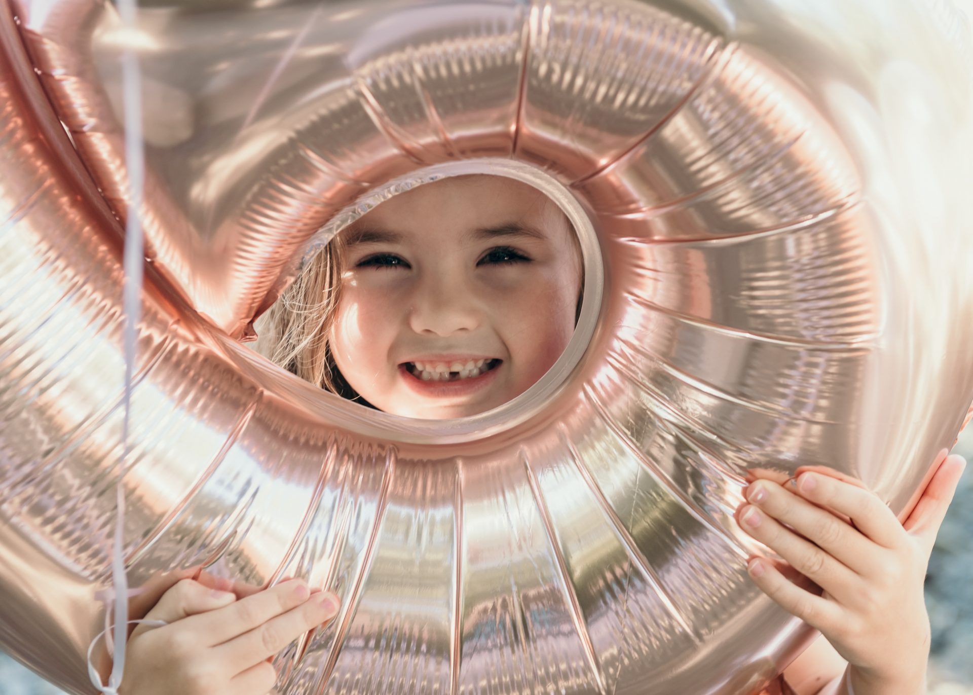 Looking through a rose gold metallic balloon with a joyful expression.