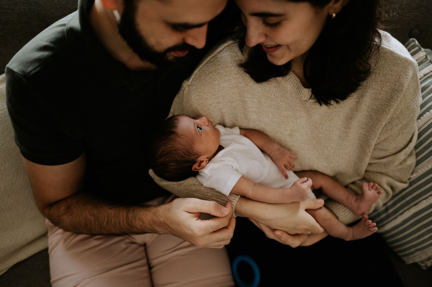 New parents lovingly hold and gaze at their newborn baby in an intimate indoor portrait.