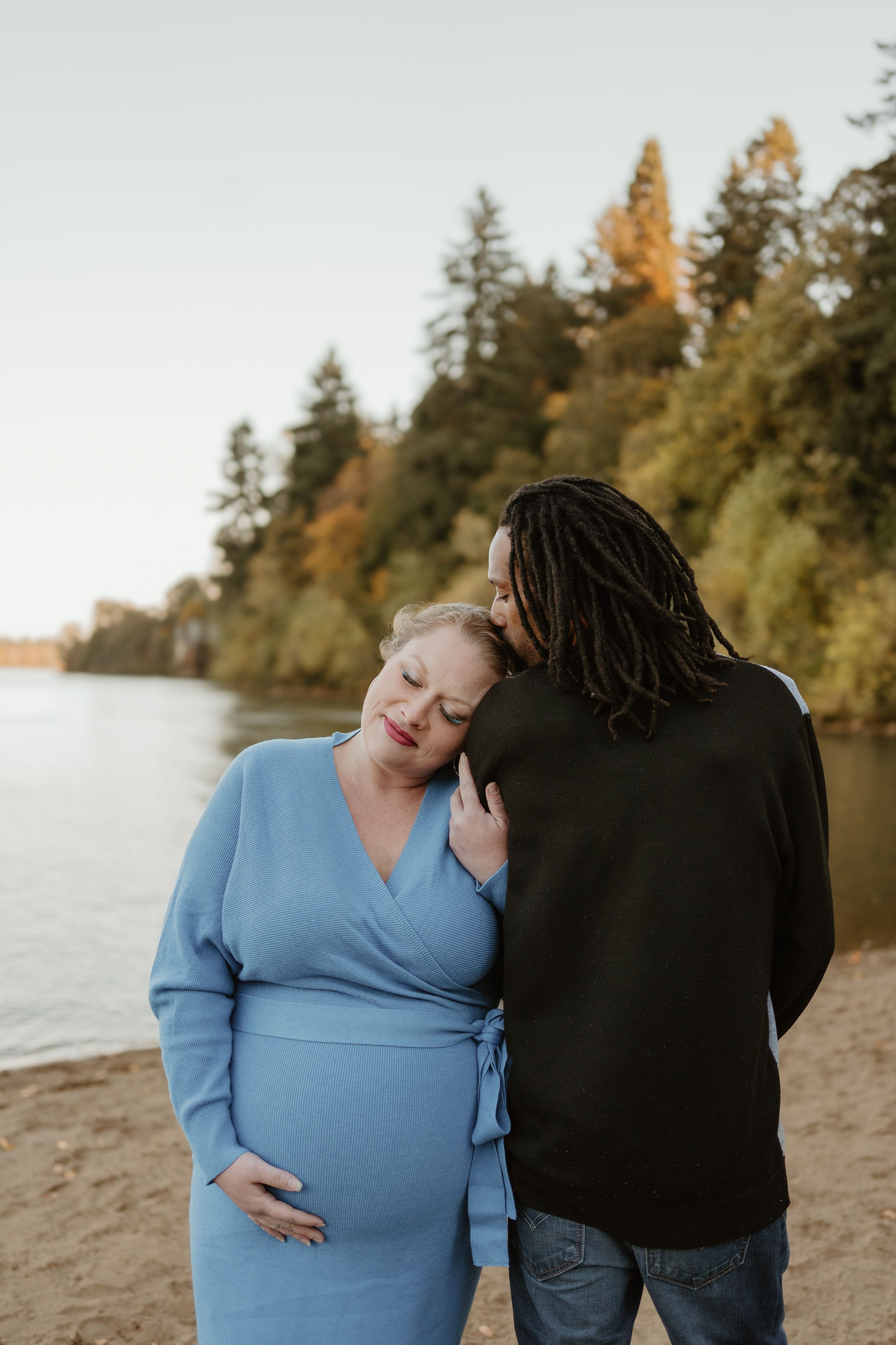Intimate couple portrait on beach with autumn trees in background.