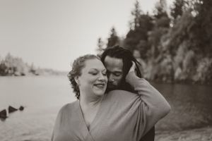 Black and white portrait of couple sharing tender moment by lakeside.