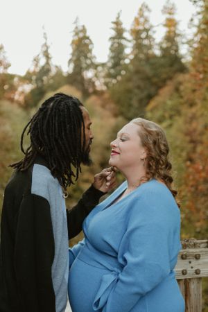 A couple shares laughter and tender moments on a deck with fall colors in the background.
