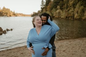 Romantic beach photoshoot with couple against waterfront and fall foliage.