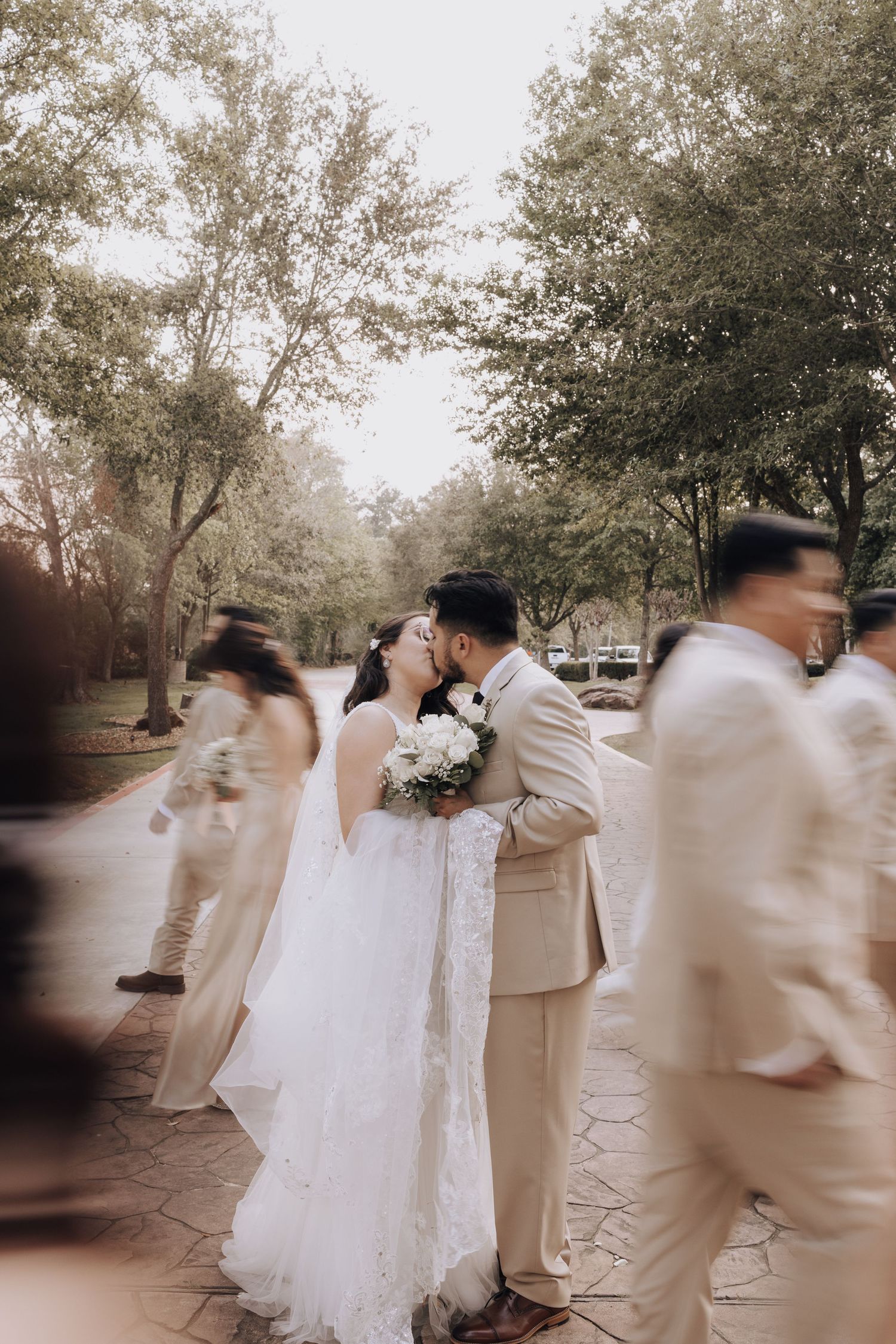 Wedding couple shares intimate moment during ceremony while guests in beige attire pass by.