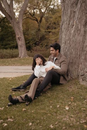 Couple relaxing together under a large tree in a park during autumn.