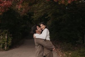 A romantic embrace captured in a wooded area with fall foliage in the background.