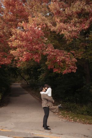 A romantic embrace beneath vibrant red maple trees along an autumn path.