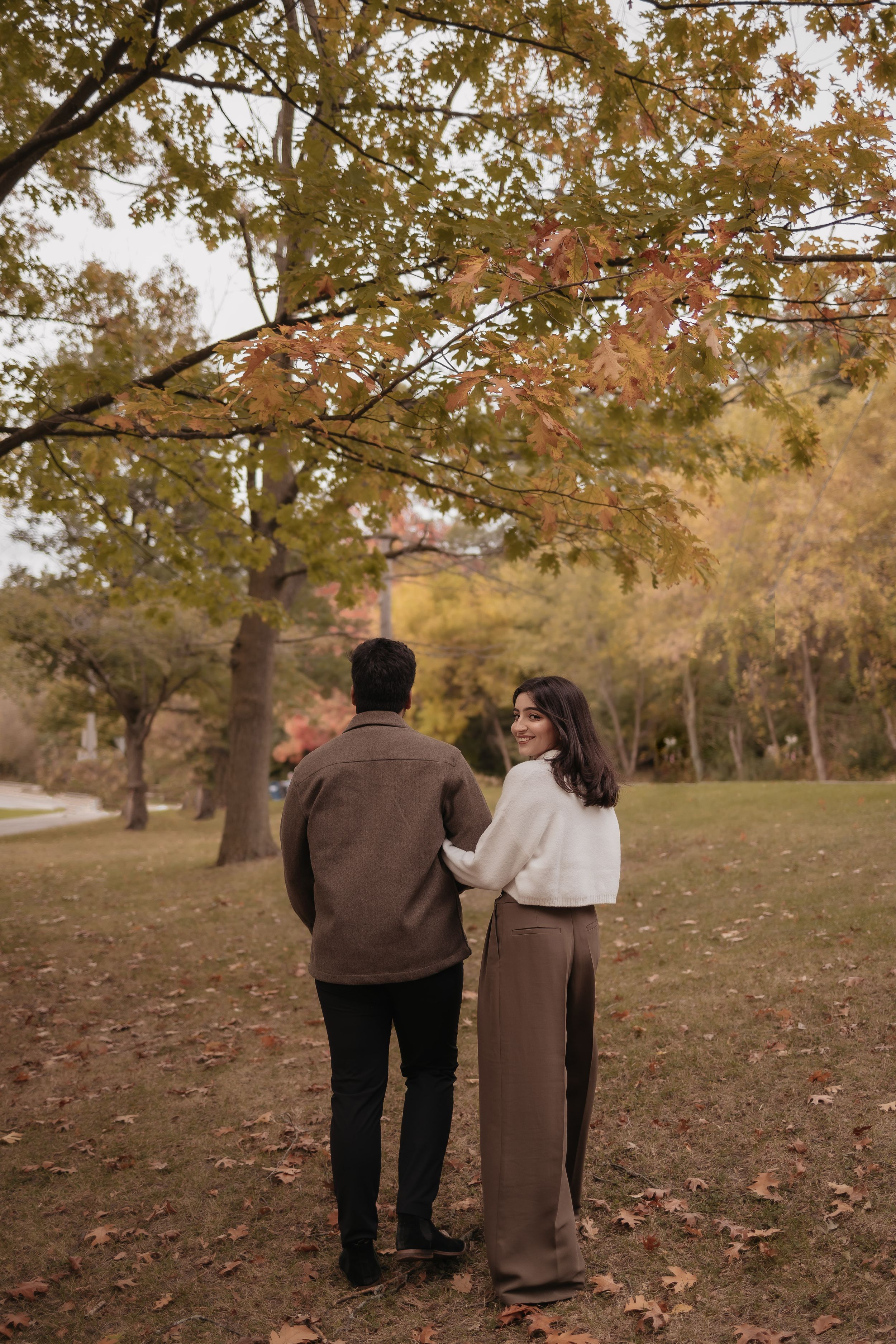 A couple strolls together under golden fall foliage in a park.