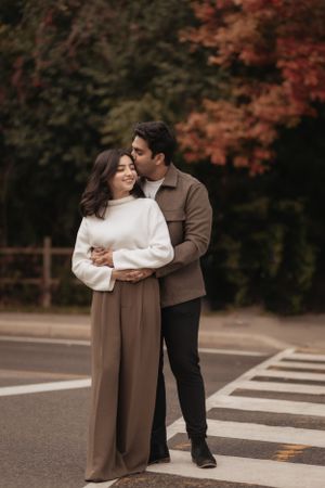A romantic autumn scene of a couple embracing on a crosswalk surrounded by fall foliage.