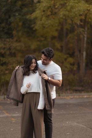 A couple sharing an intimate moment in a parking lot with fall trees in the background.