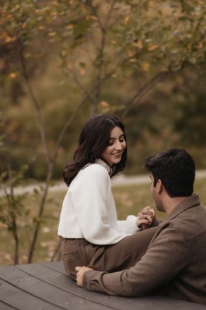 A couple sharing a sweet moment while sitting at a wooden picnic table in a park.