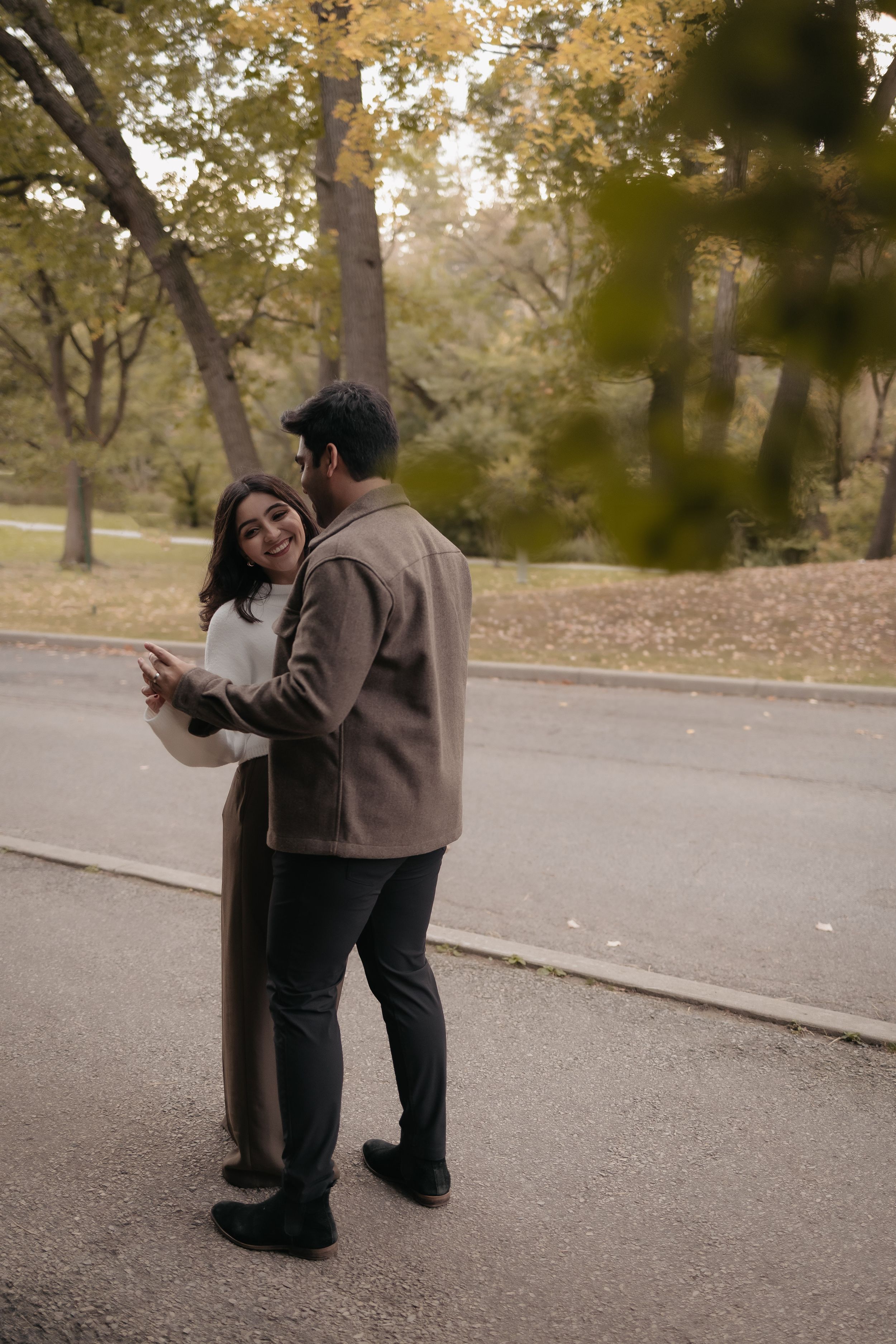 A couple standing close together on an autumn street looking at something together.