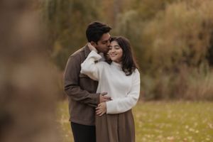 A tender moment between a couple in coordinated neutral outfits against an autumn backdrop.