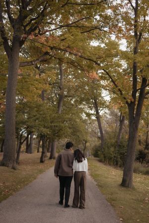 A couple walking hand in hand down a tree-lined path with golden autumn leaves overhead.