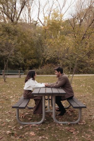 Couple sitting at picnic table in autumn park having conversation.