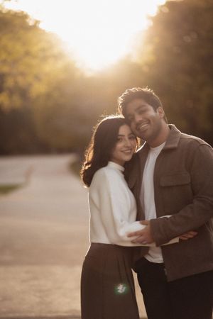 A couple laughing together in golden sunset light with autumn trees behind them.