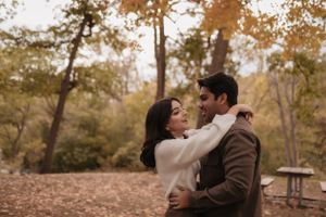 Two people share an intimate moment amidst fallen autumn leaves in a park.