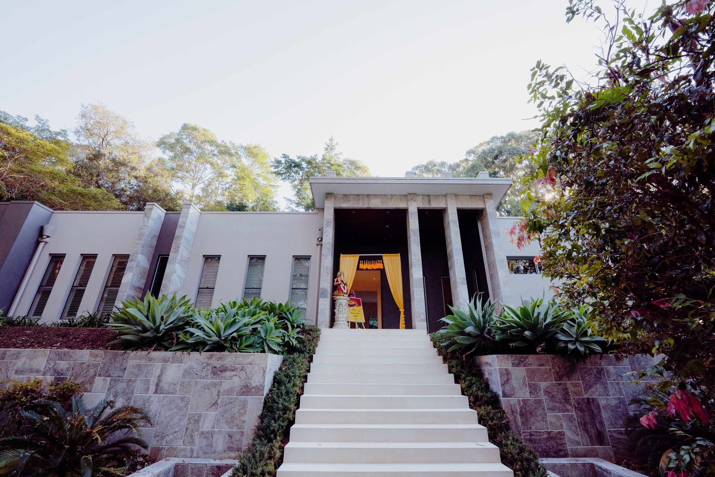 Elegant modern house entrance with white stone steps and tropical landscaping.