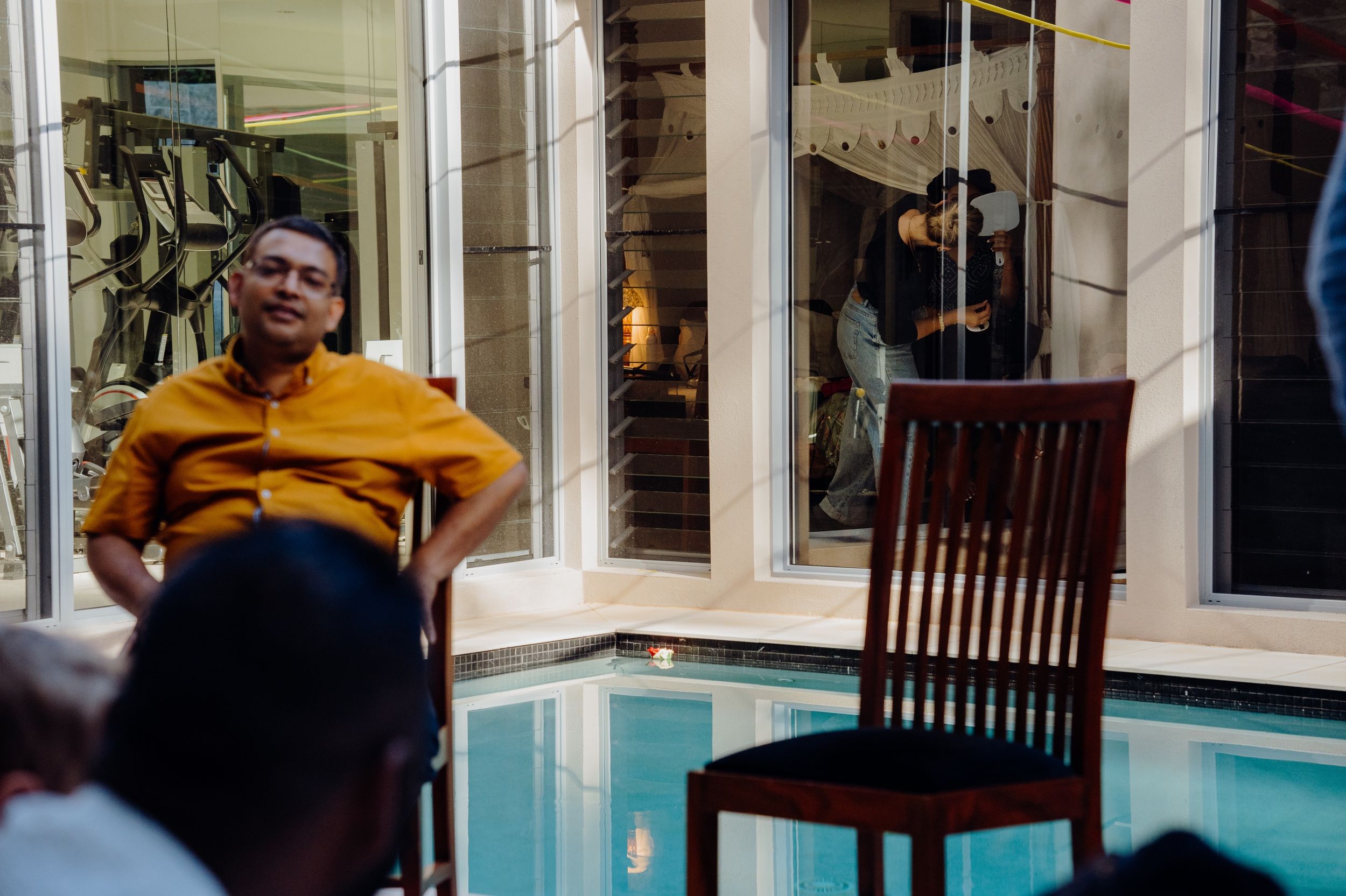 Person in bright yellow shirt sitting by indoor pool with wooden chair beside them.