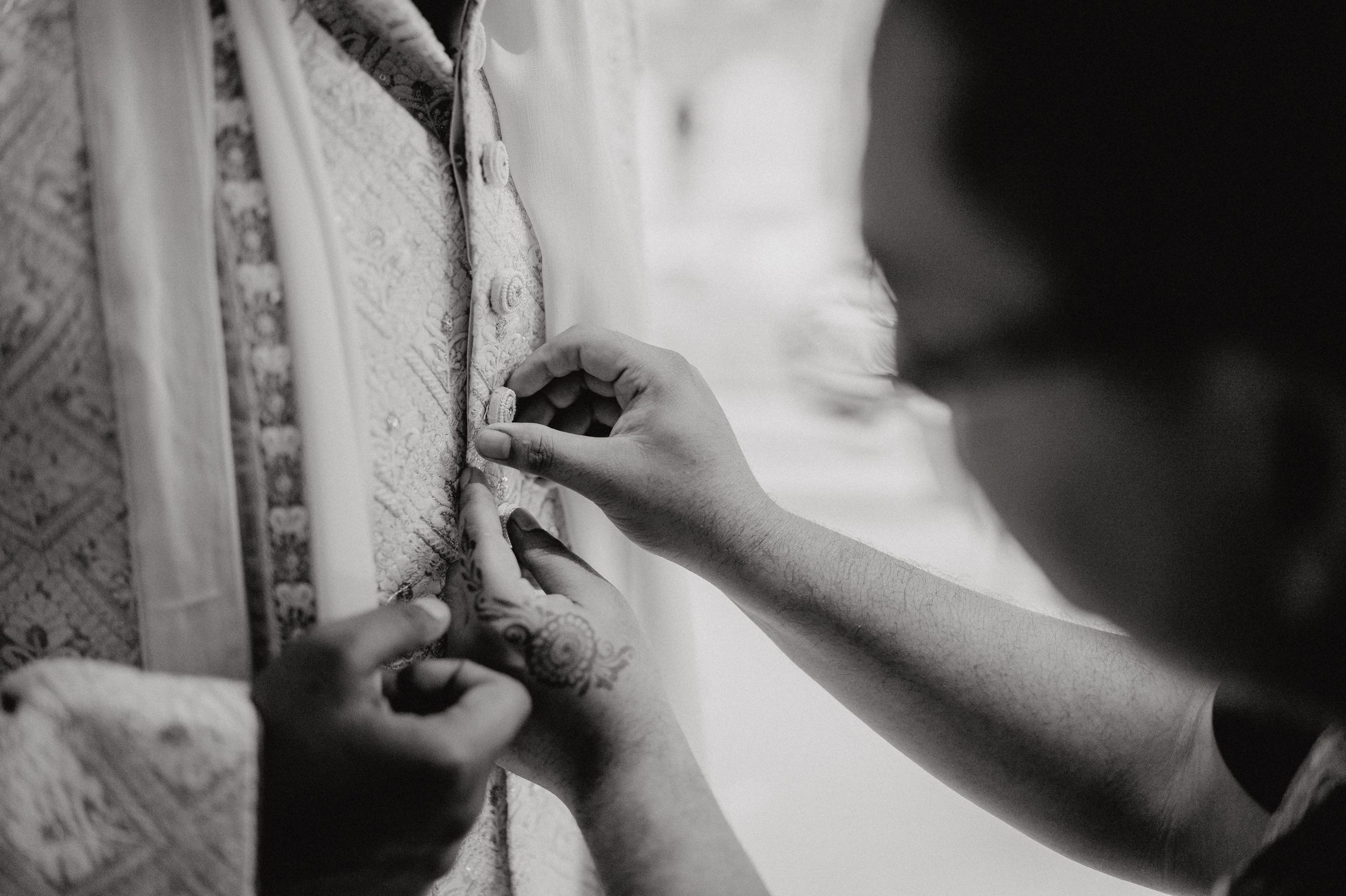 Close-up black and white shot of hands adjusting traditional ceremonial attire.
