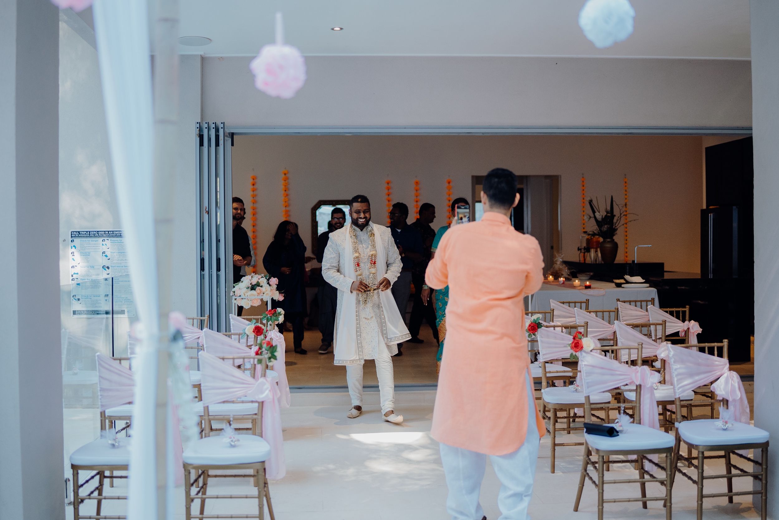 An indoor wedding venue with white chairs and pastel decorations being set up for a ceremony.