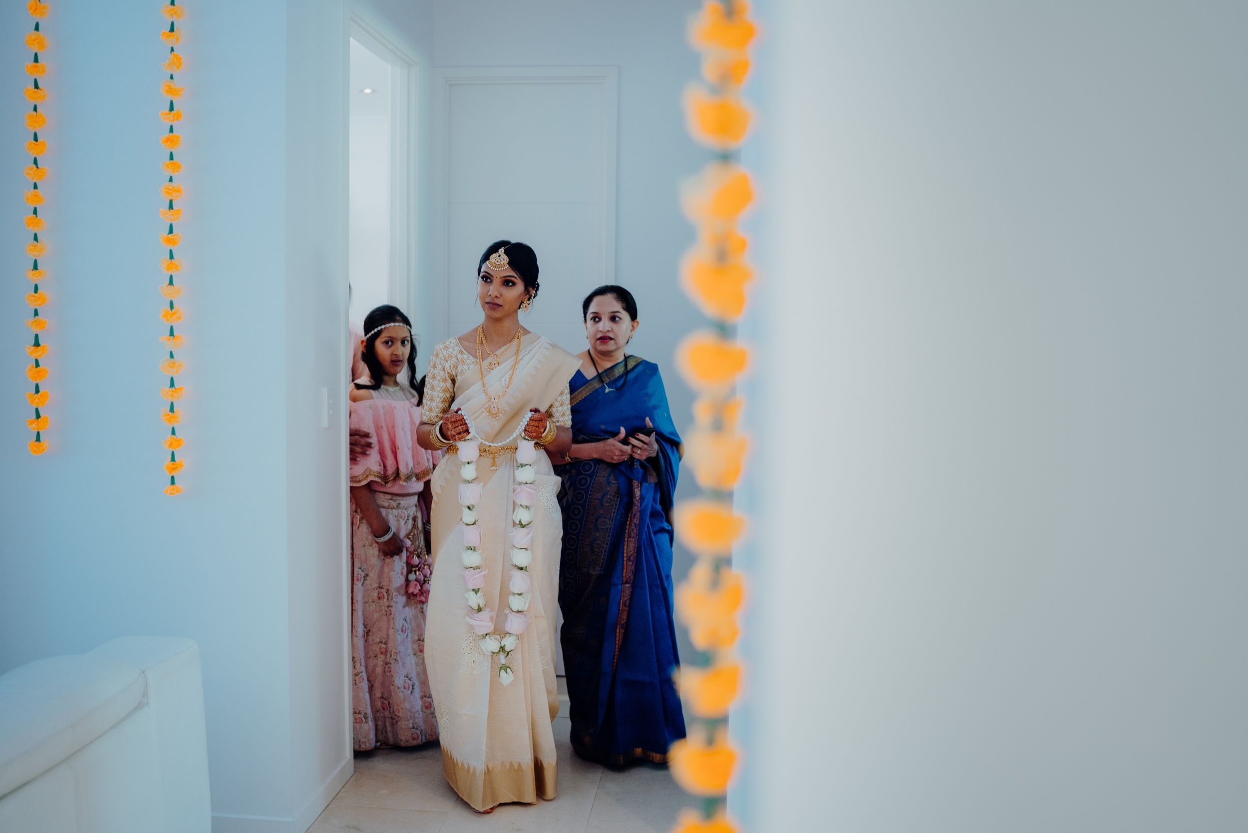 People standing in a hallway decorated with orange marigold garlands for a cultural celebration.