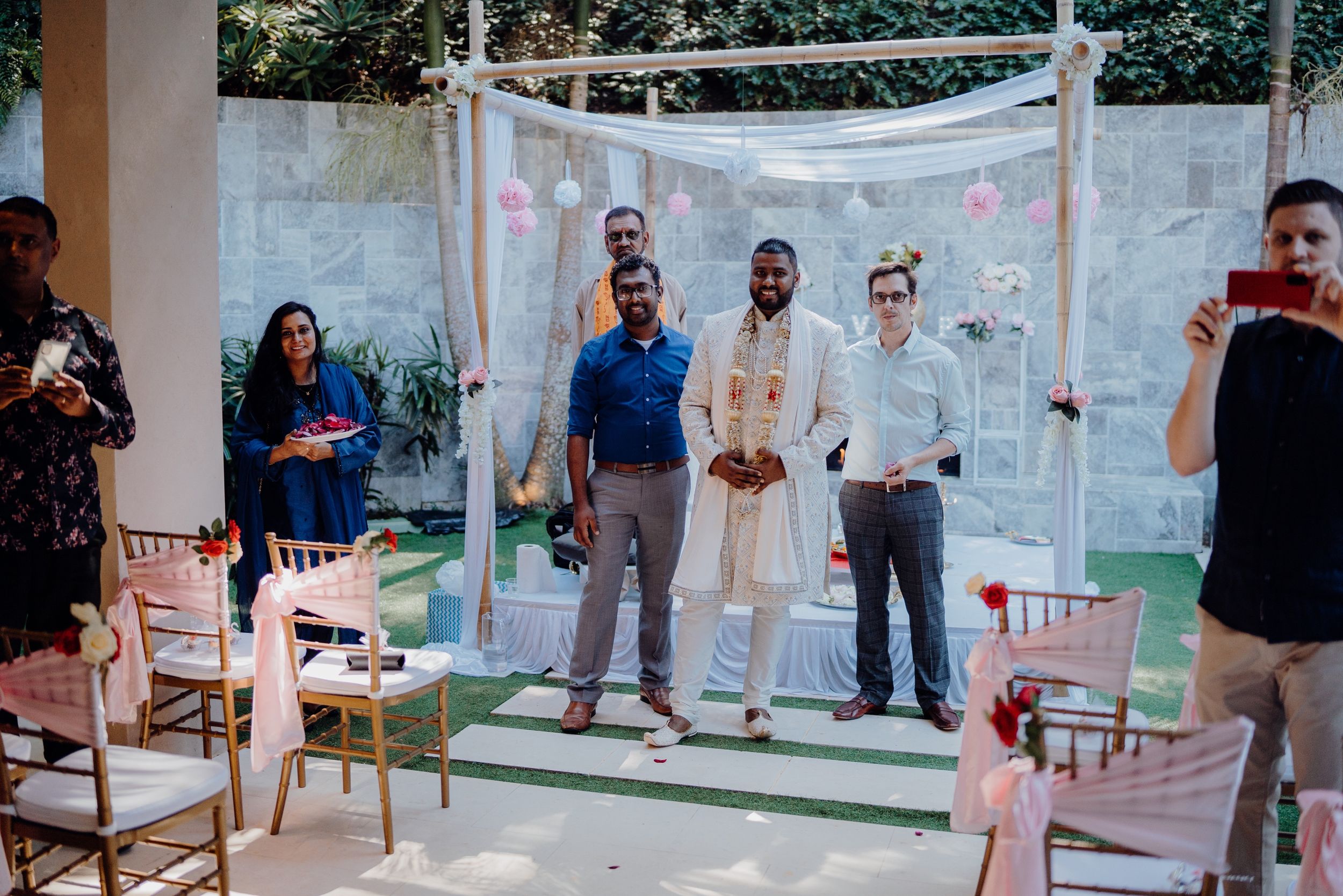 Outdoor wedding ceremony space with white canopy, pink accents, and wooden chairs arranged for guests.