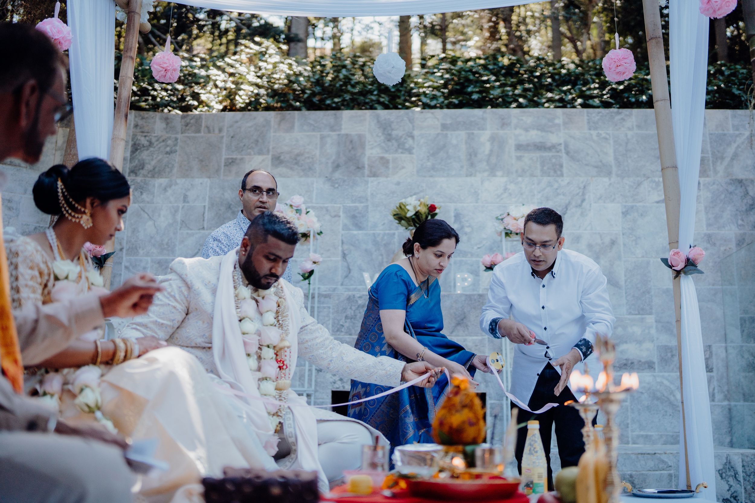 Wedding ceremony participants seated under white canopy with traditional decorations and candles.