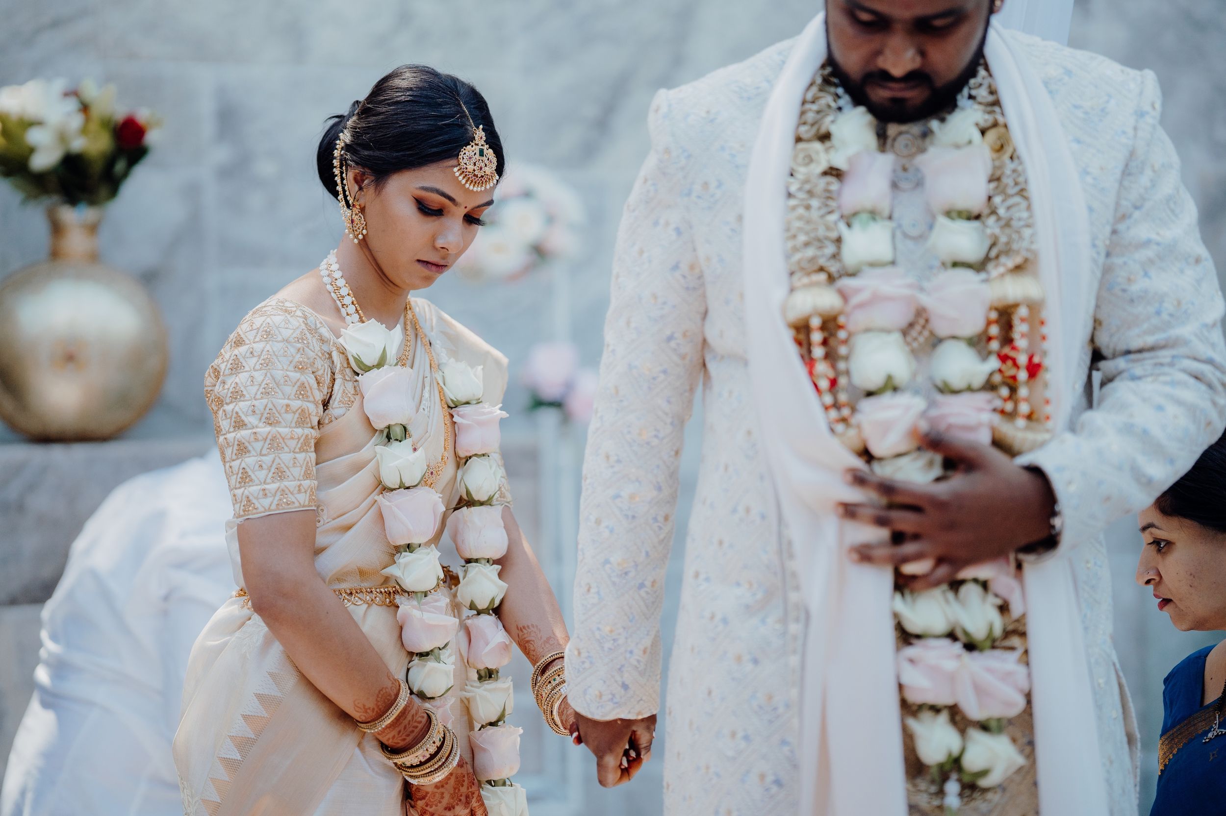 Traditional Indian wedding couple wearing white outfits and floral garlands during ceremony.