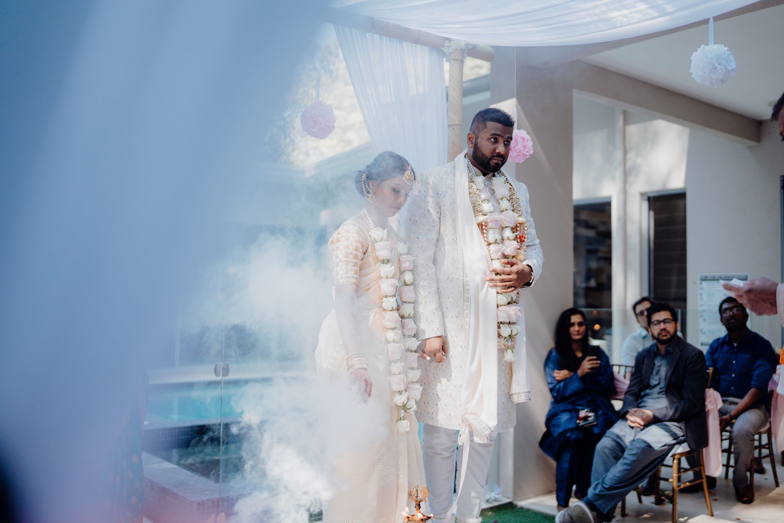 Wedding ceremony under white draped canopy with guests seated in background.