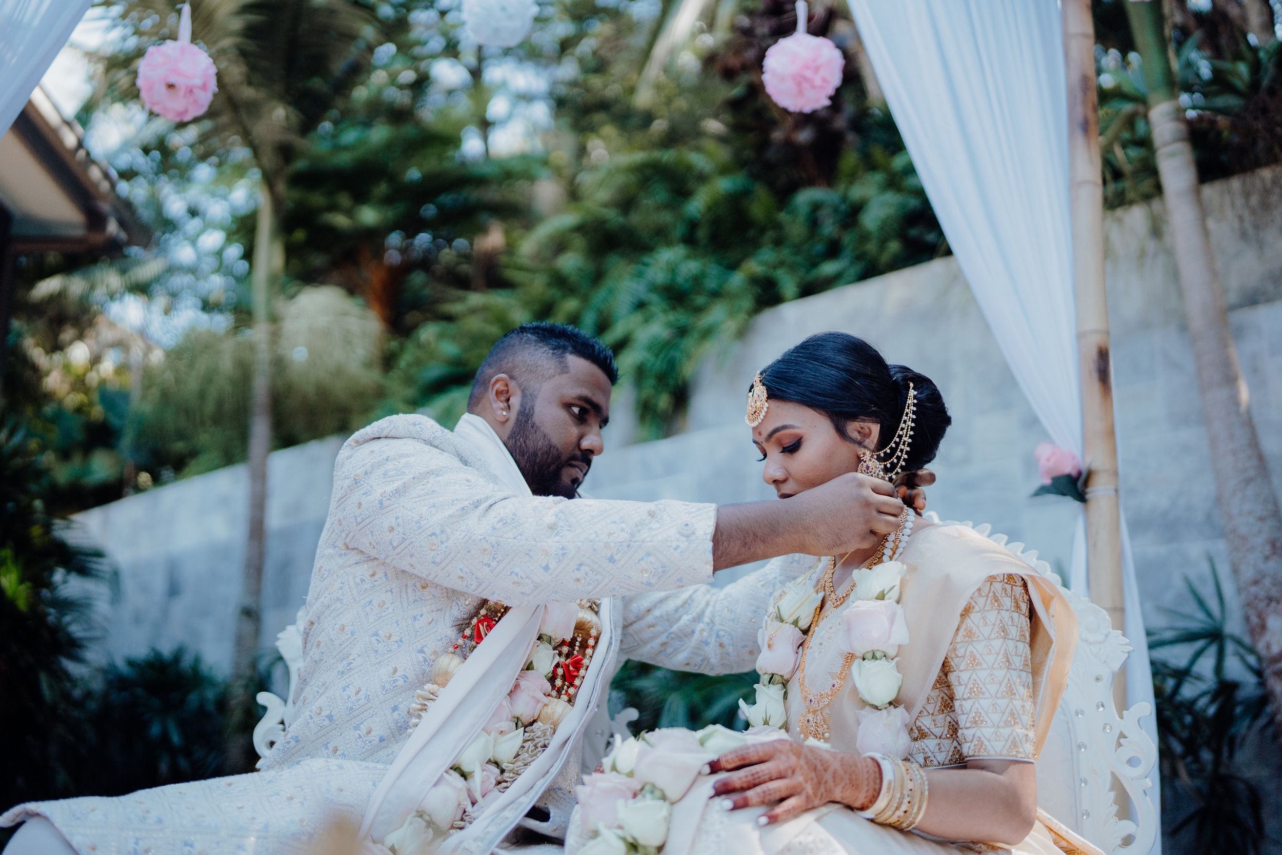 A tender moment during a wedding ceremony under a white canopy with pink decorations.