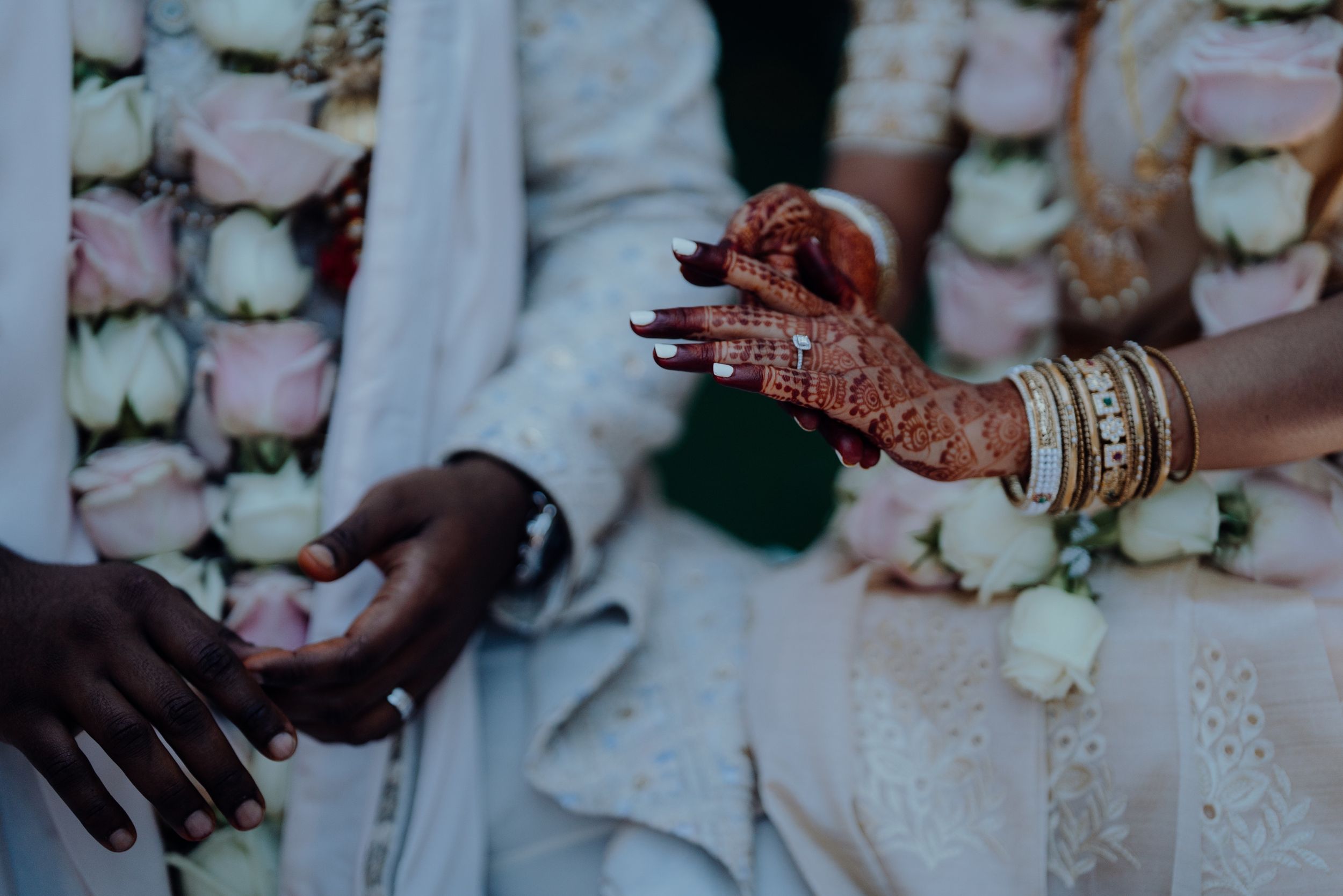 Hands adorned with henna and bangles during a wedding ceremony exchange.