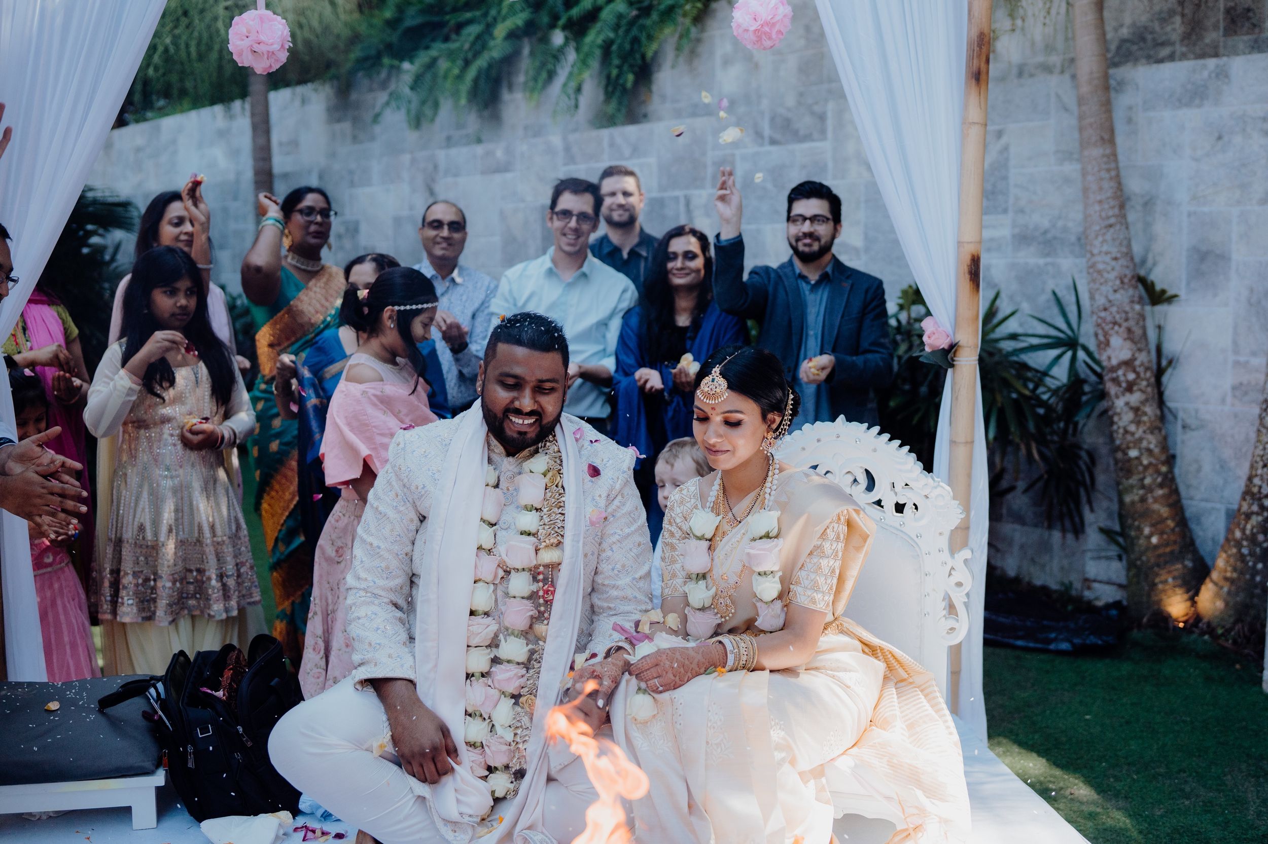 An outdoor wedding ceremony with guests watching the couple under pink balloon decorations.