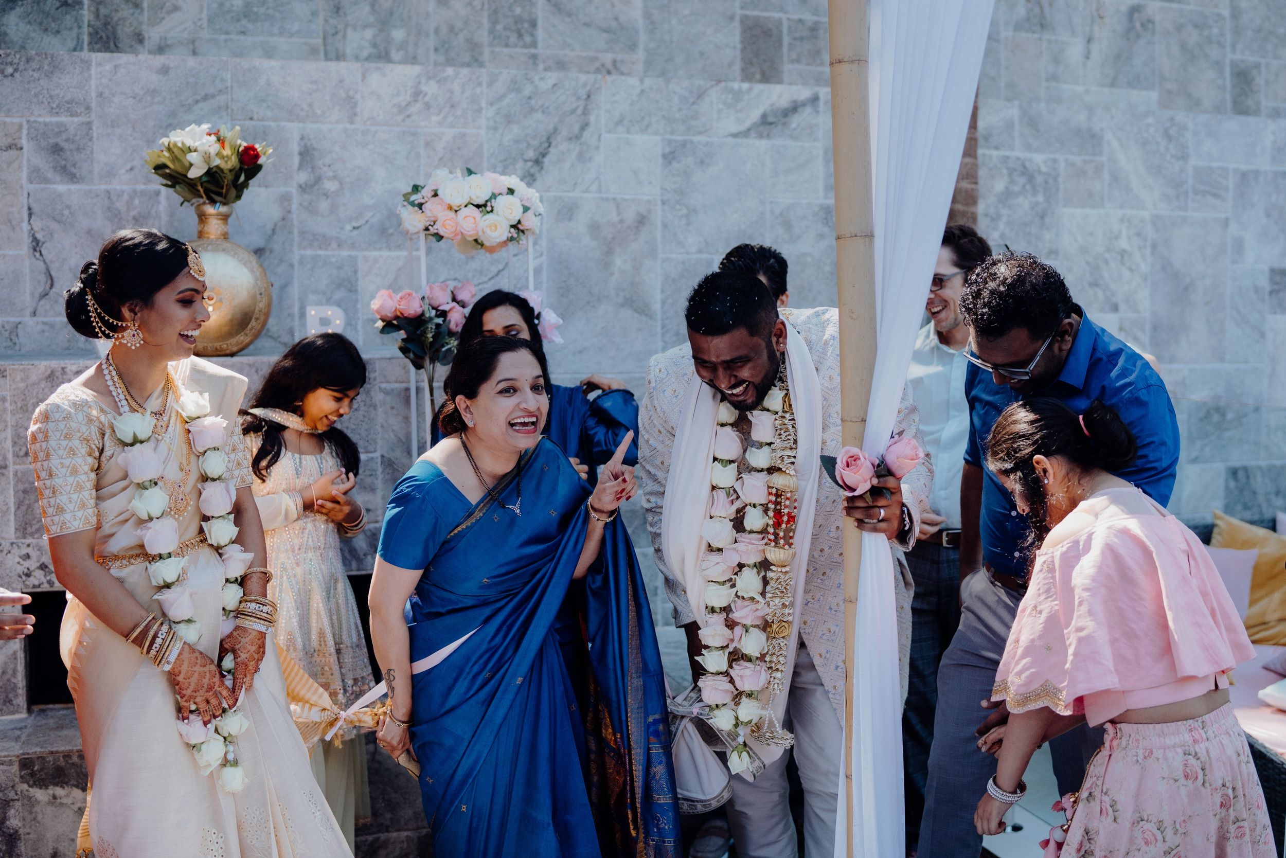 Guests in traditional attire gather around during a multicultural wedding ceremony with floral garlands.