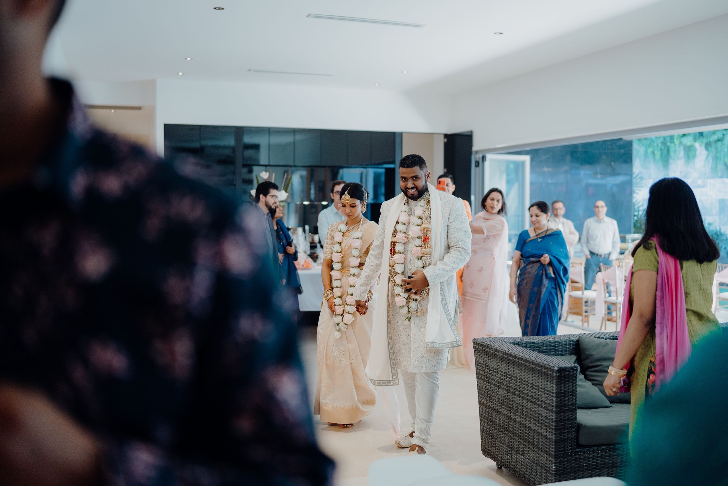 Wedding guests gather in an elegant room to celebrate as a couple walks down an aisle.