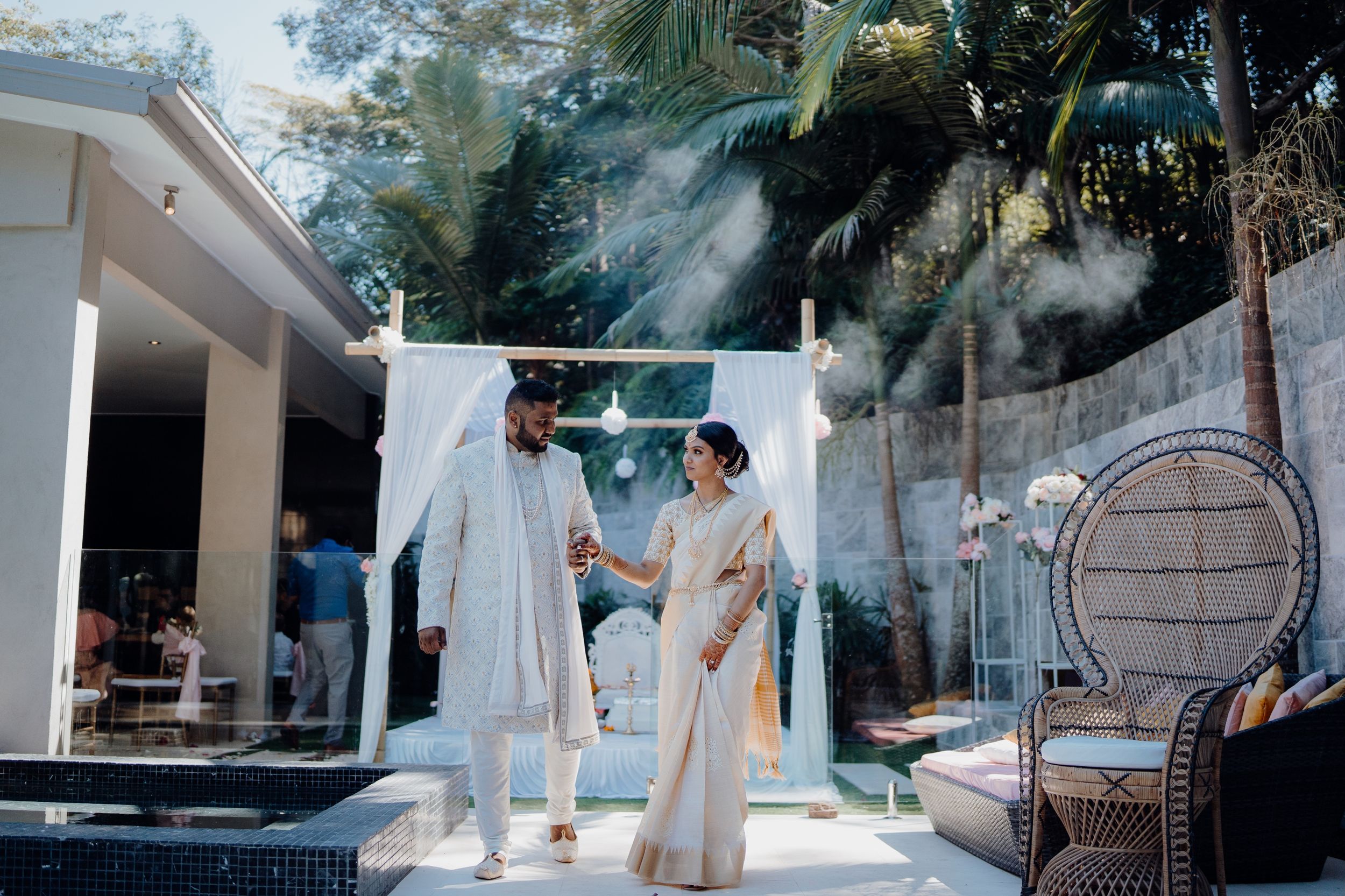 A couple shares an intimate moment outdoors amid smoke effects and tropical landscaping.