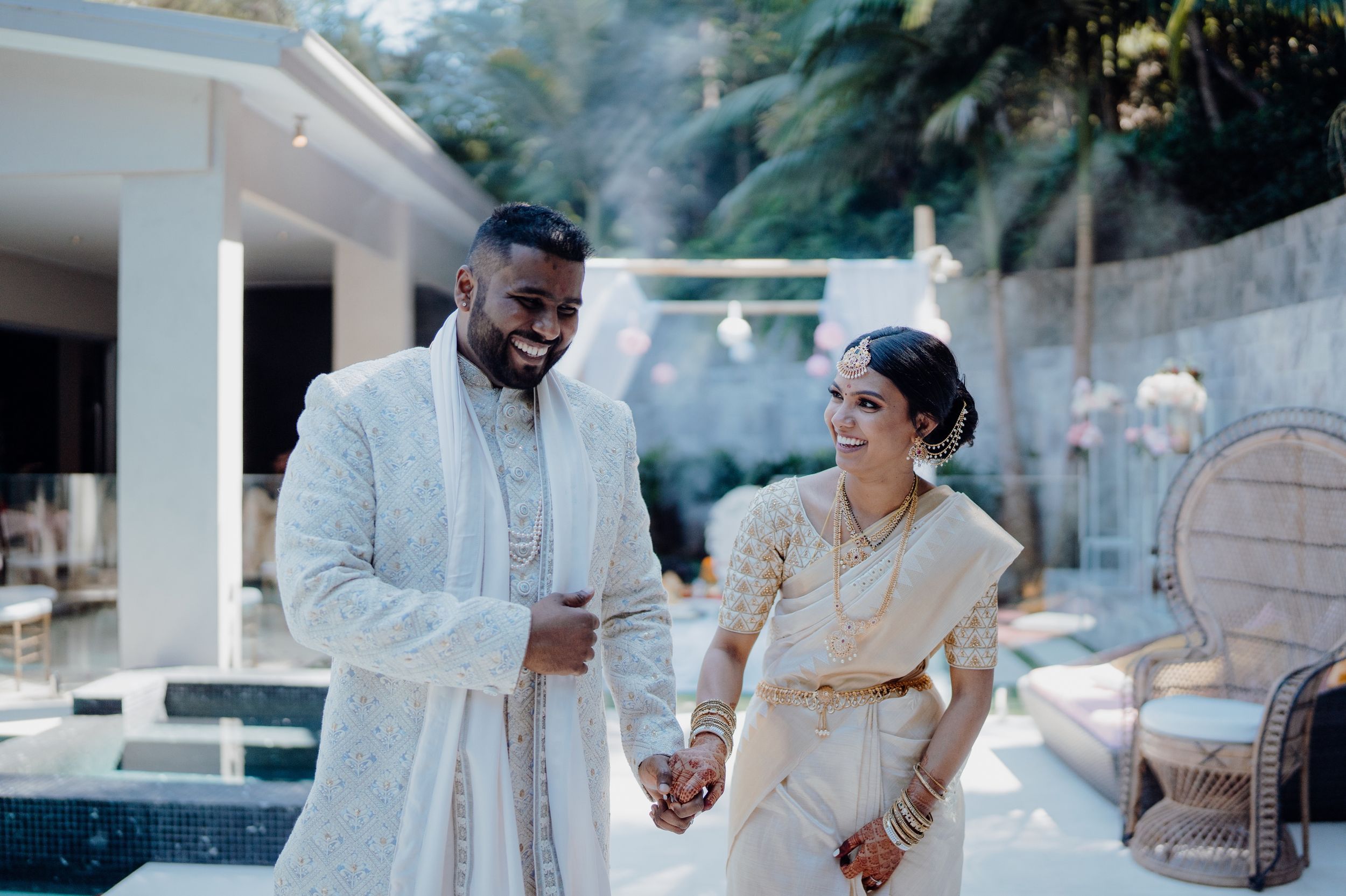 A wedding couple enjoys a light-hearted moment by a pool in traditional attire.
