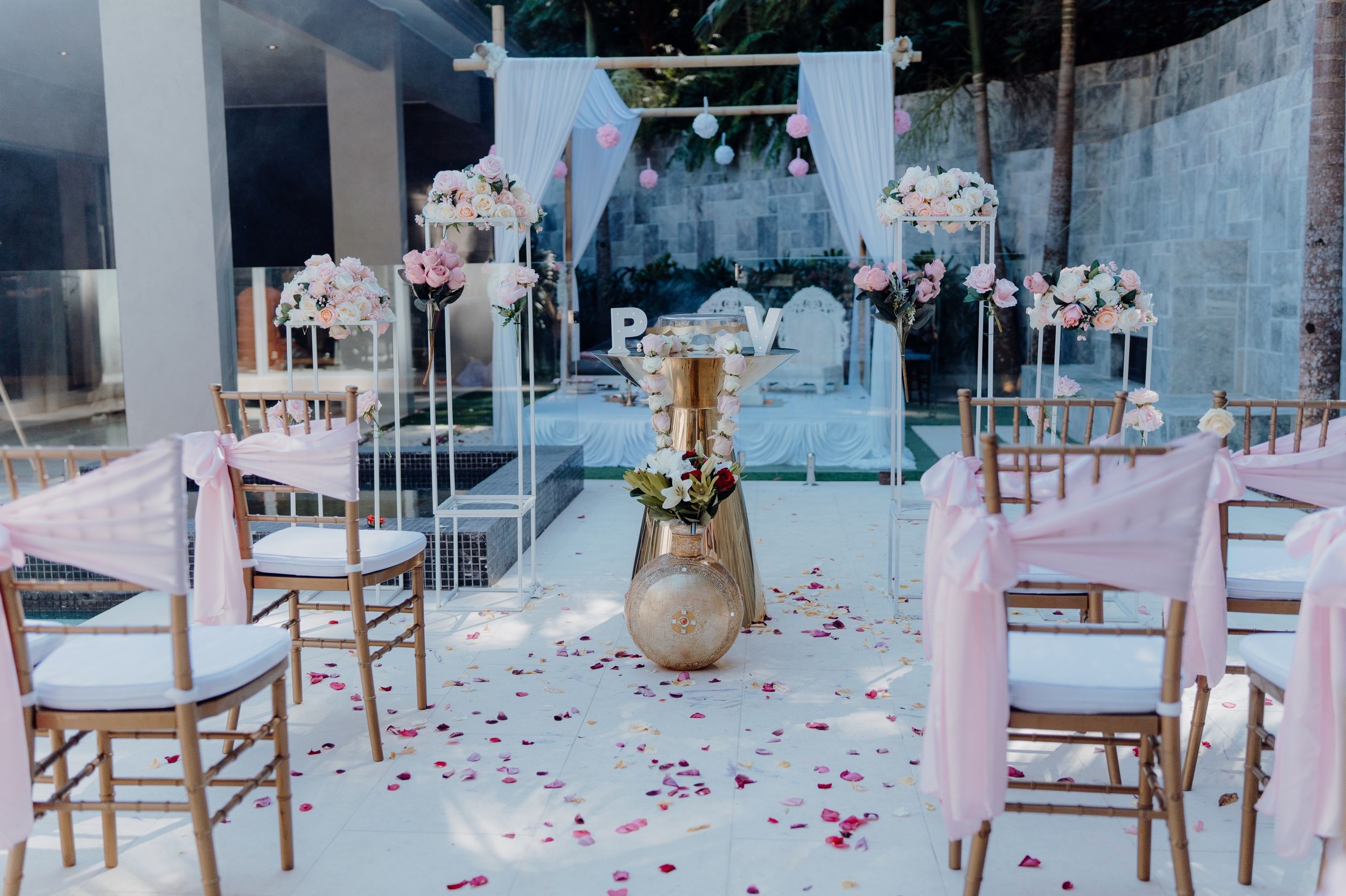 Elegant wedding ceremony setup with white chairs, pink flowers and rose petals scattered along the aisle.