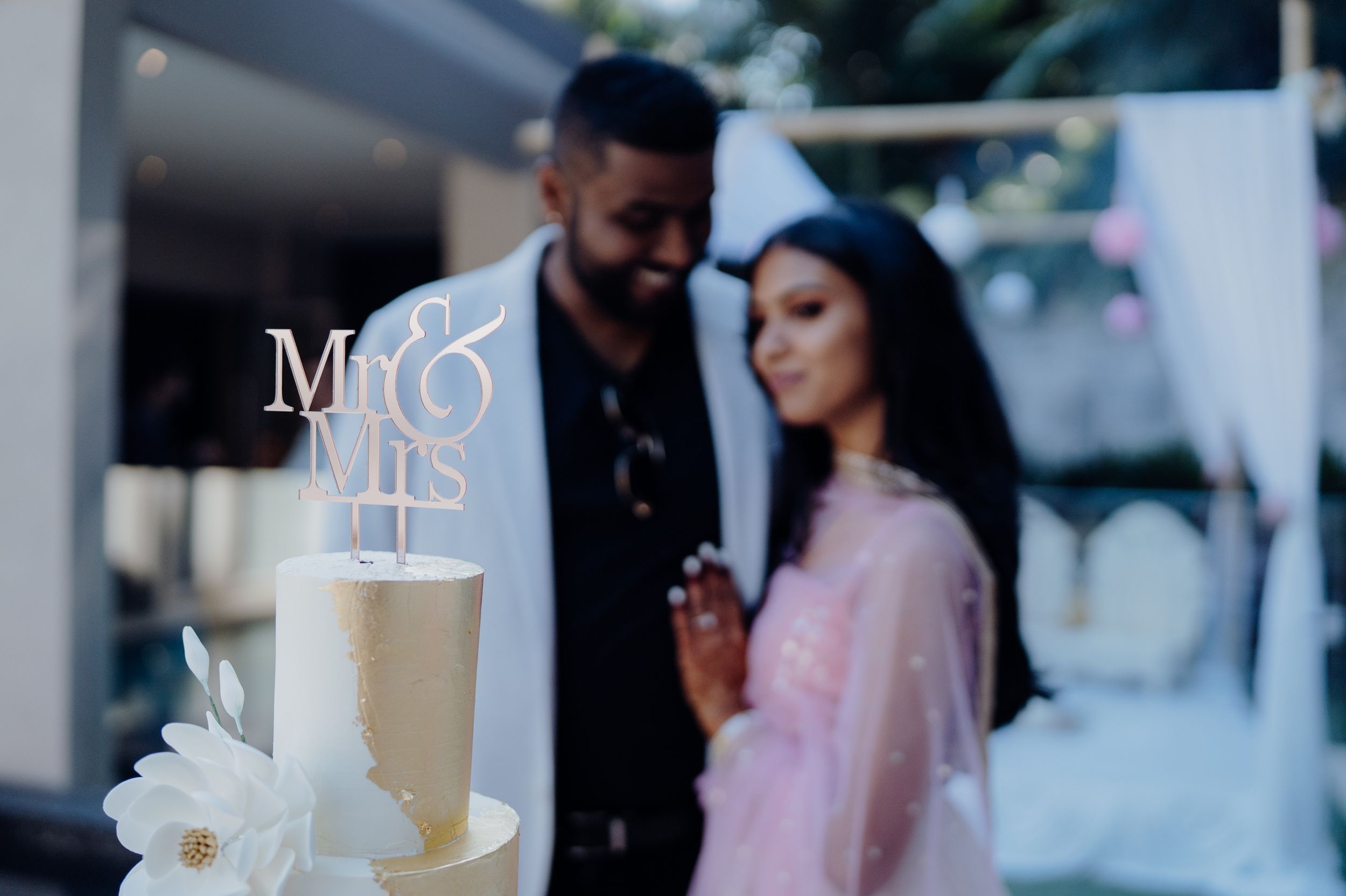 Wedding cake display with Mr and Mrs topper and white floral decorations against a blurred background.