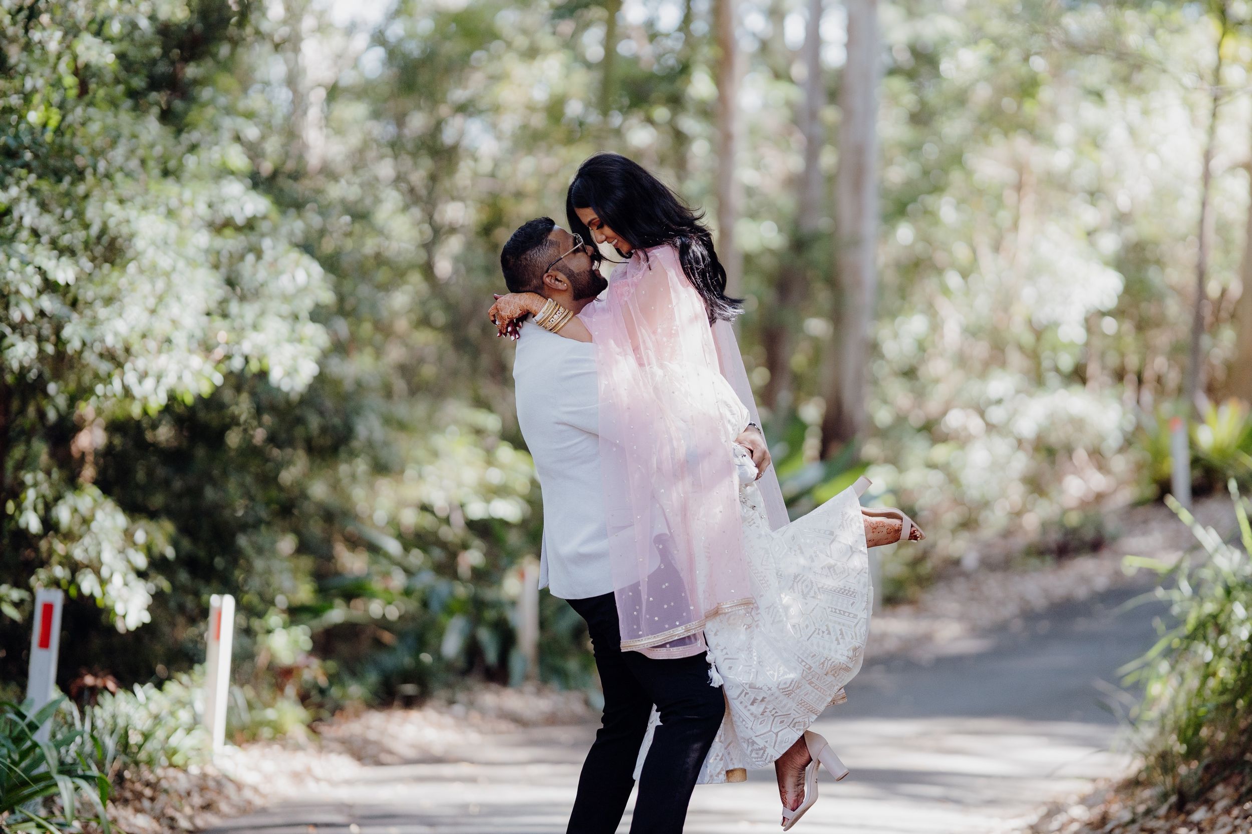 Romantic moment captured on a tree-lined garden path during wedding photoshoot.