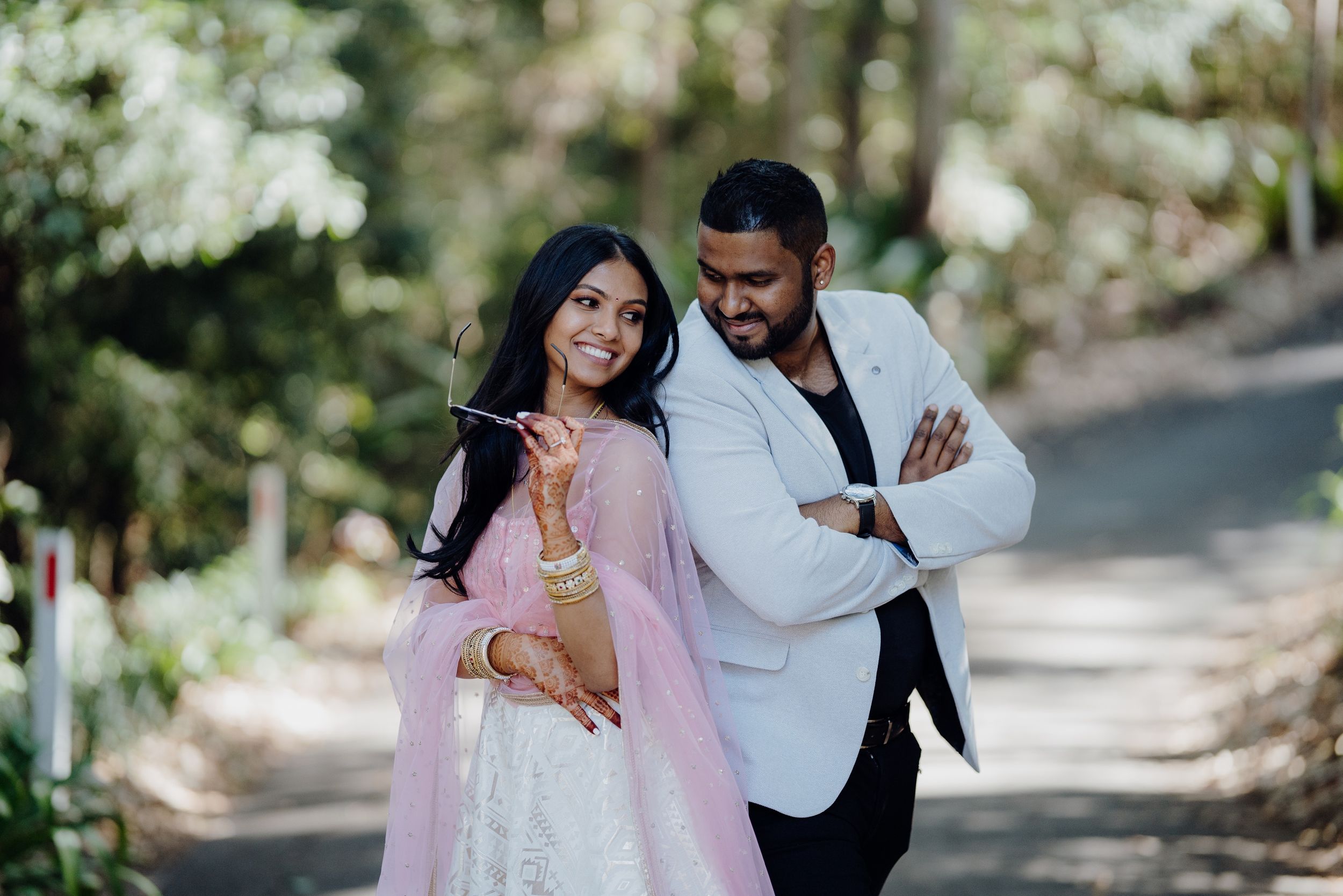 Candid moment between couple on tree-lined path during wedding photoshoot.