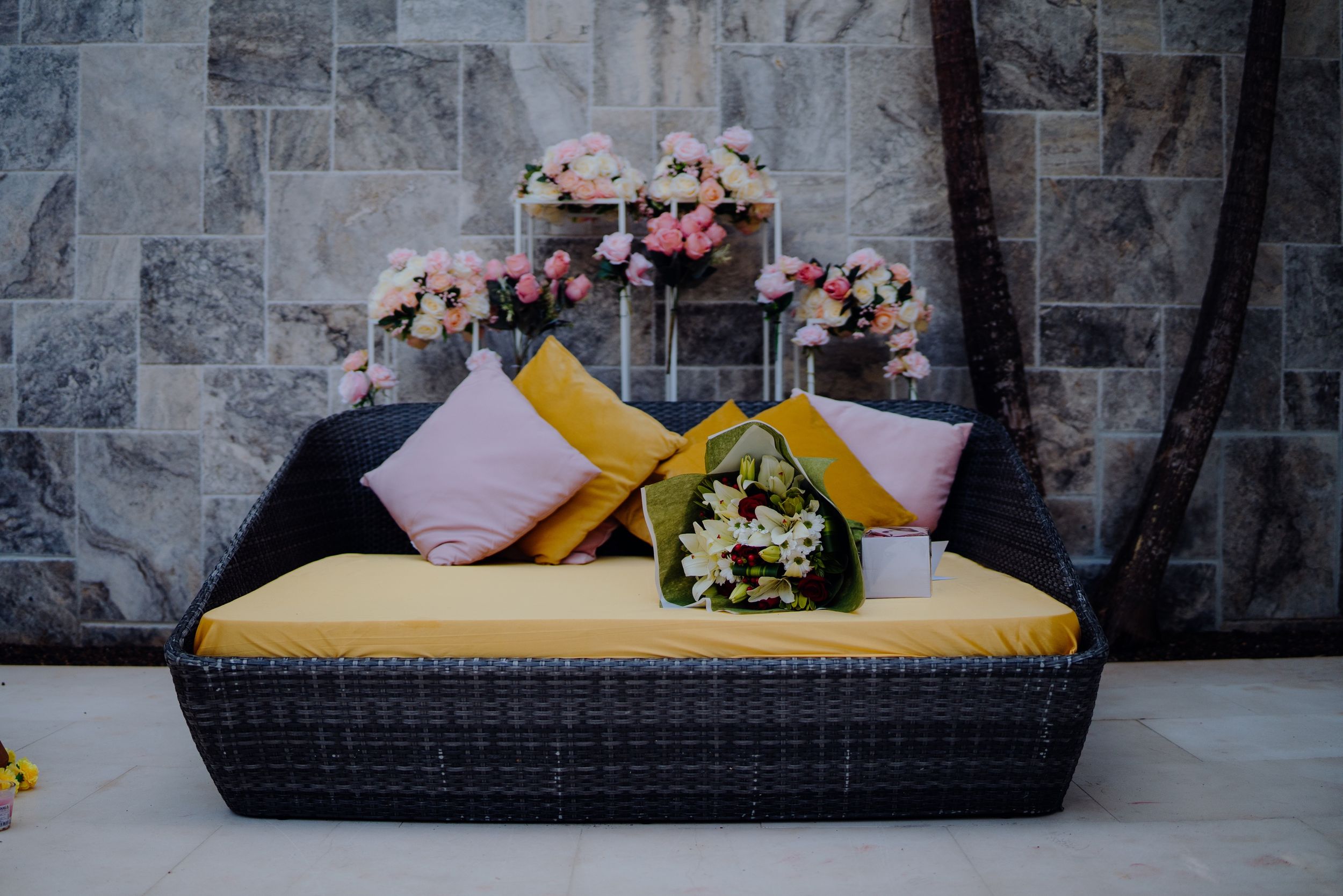 Decorative seating area with floral arrangements and yellow cushions against a stone wall.