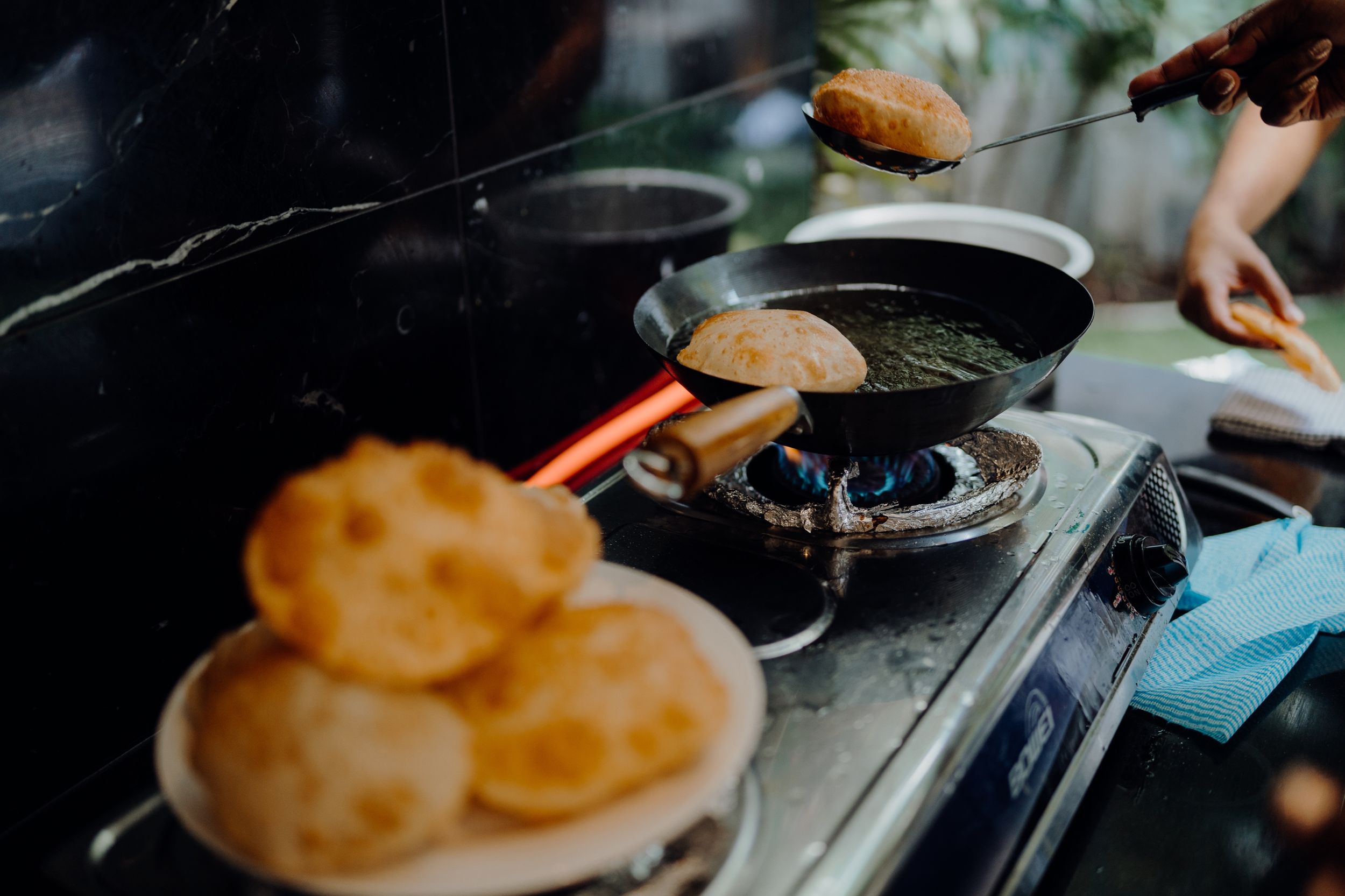 Cooking puri or flatbread on a stovetop with golden brown bread visible.