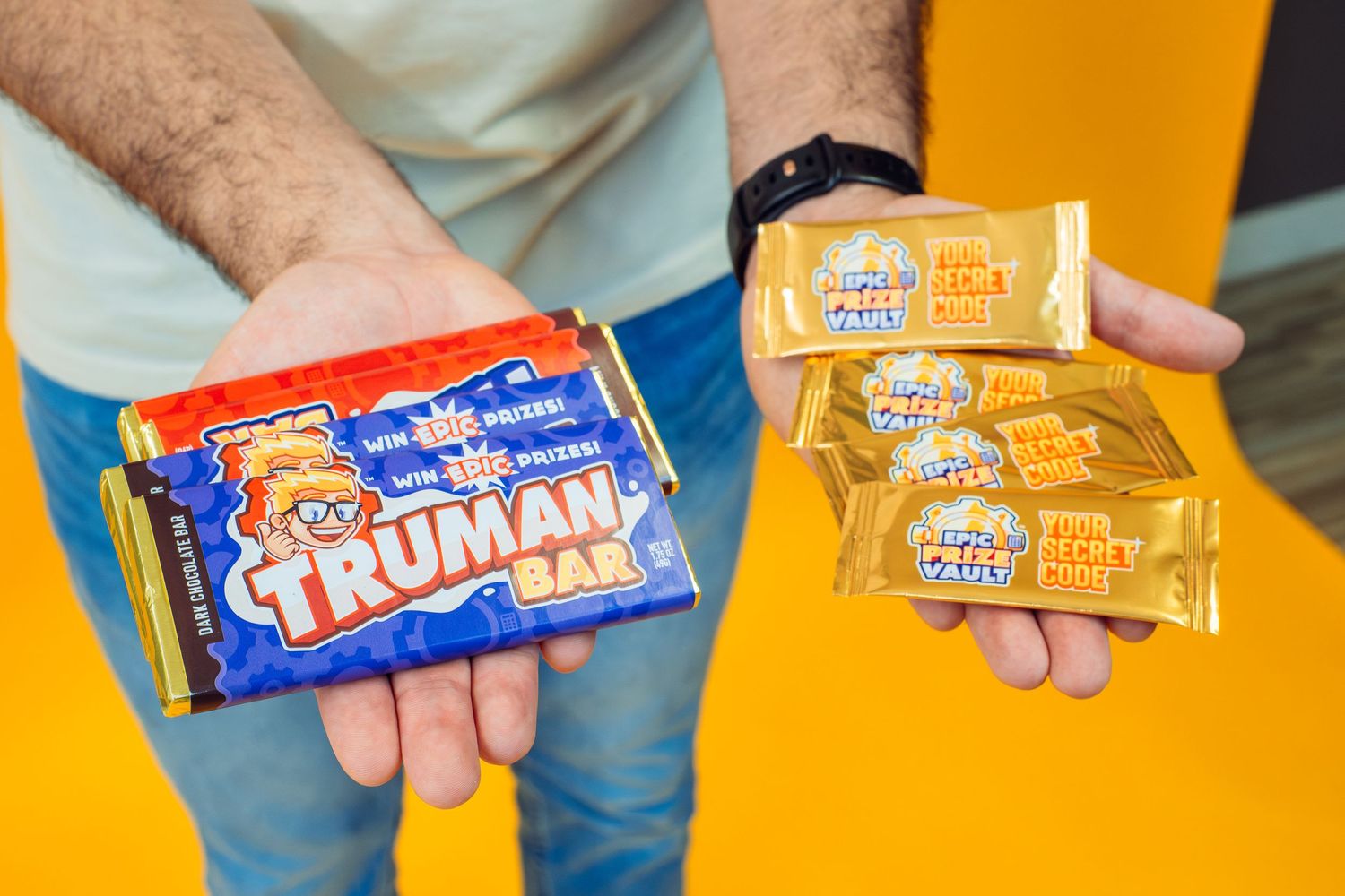 Hands holding Truman candy bars against a vibrant orange background.